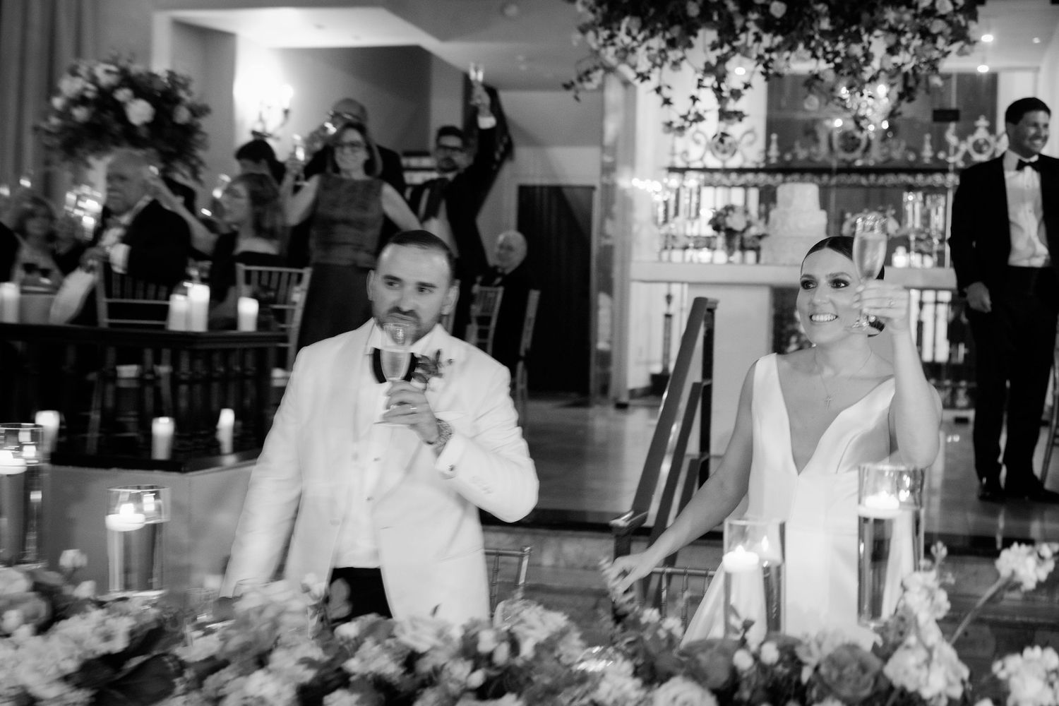 Black and white photo of wedding reception toasts with candlelit table decor.