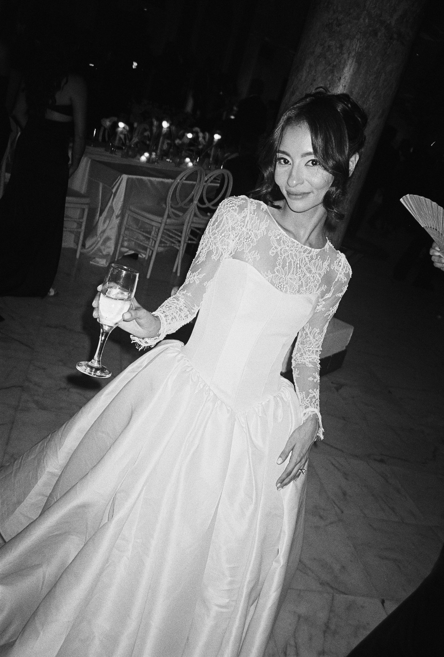 Woman in elegant white lace ball gown holding champagne glass at formal evening event, black and white photo.