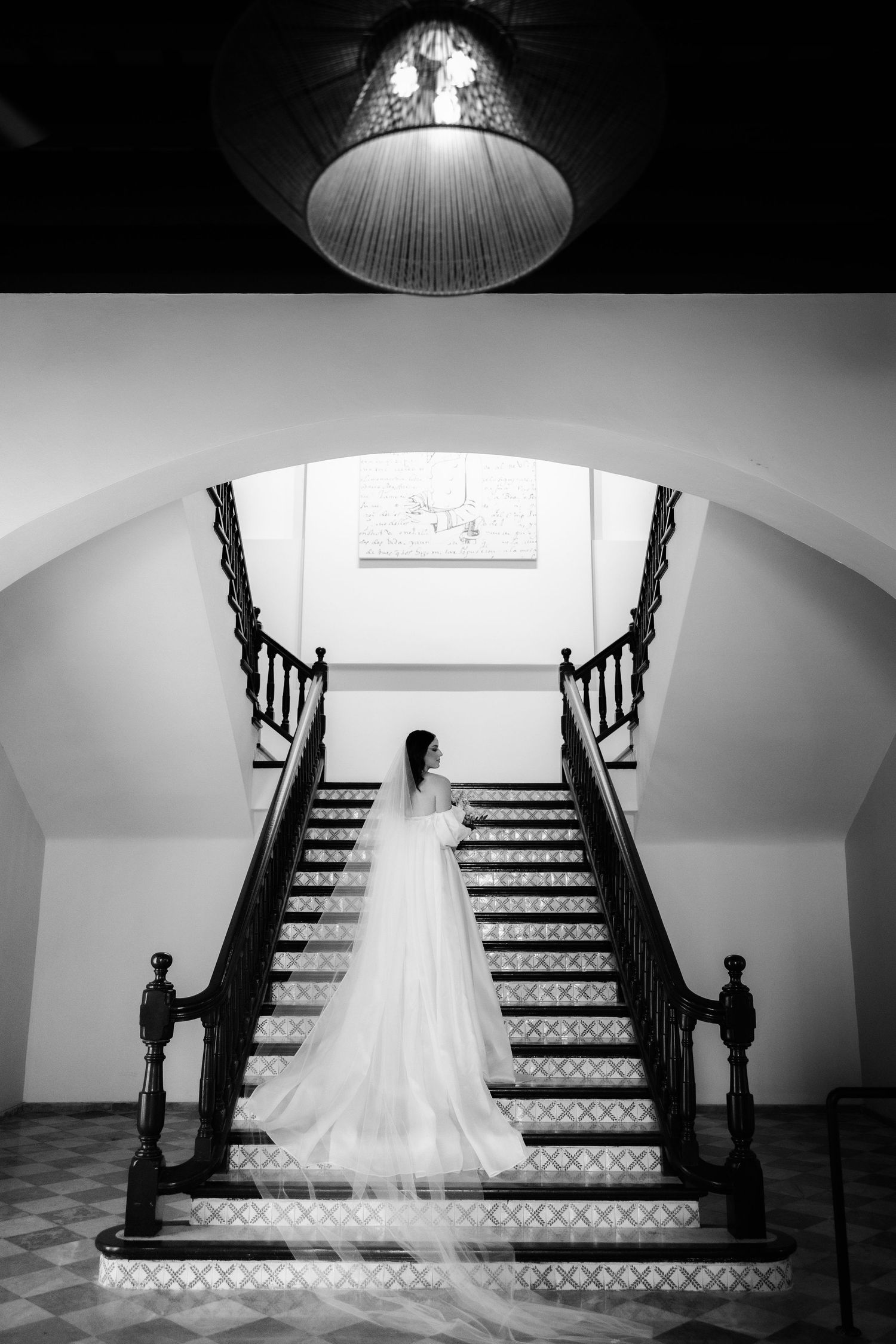 A white wedding dress displayed dramatically on a grand staircase with black railings in black and white photography.