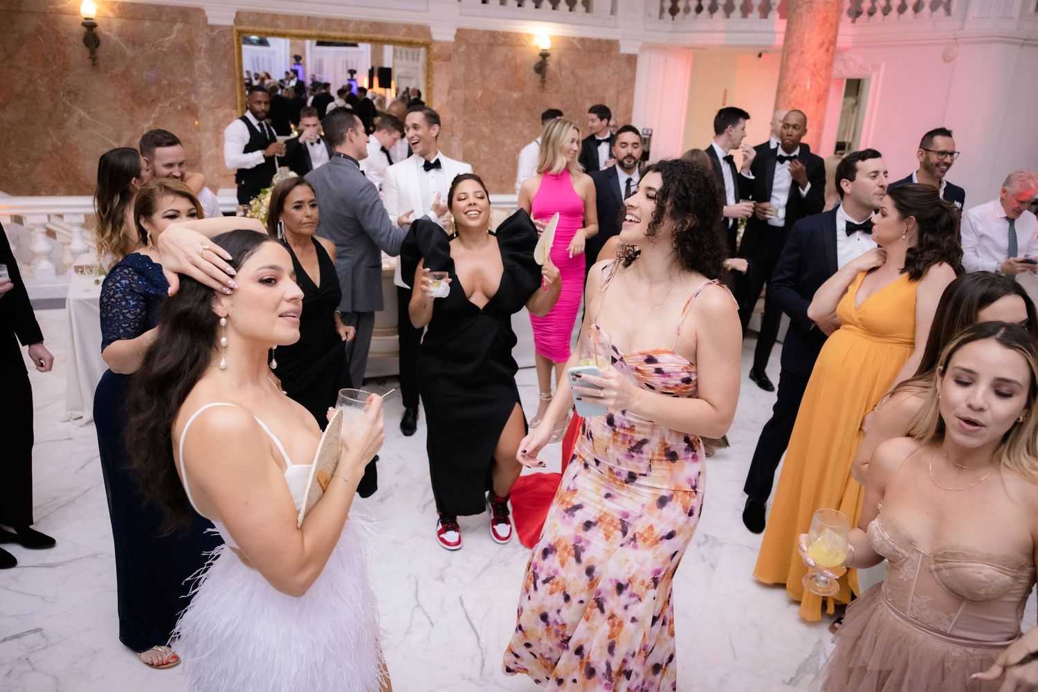 Guests dancing and celebrating together at an elegant indoor wedding reception with pink ambient lighting.
