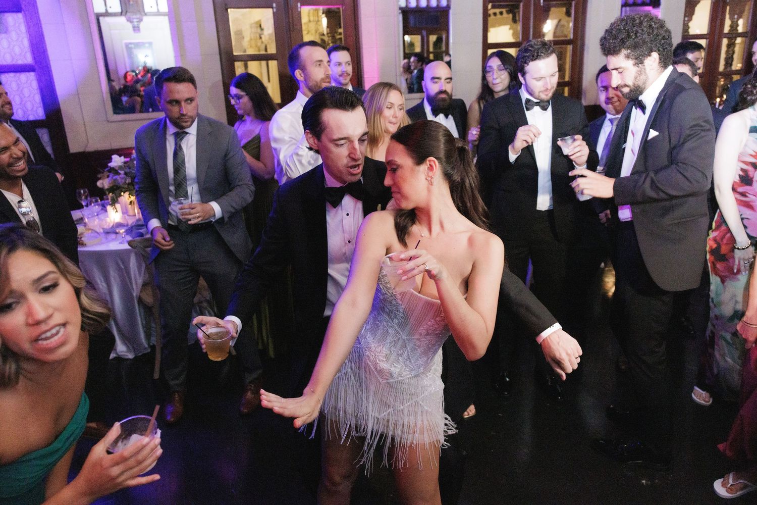 People dancing and socializing at an elegant event with formal attire and purple lighting in the background.