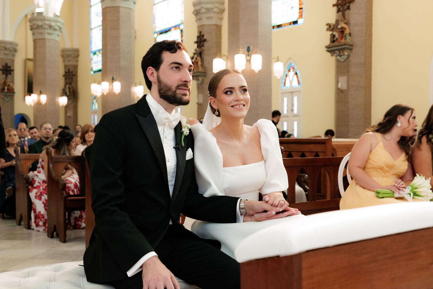 A group celebrates in formal attire during a joyful wedding ceremony at an elegant church venue.