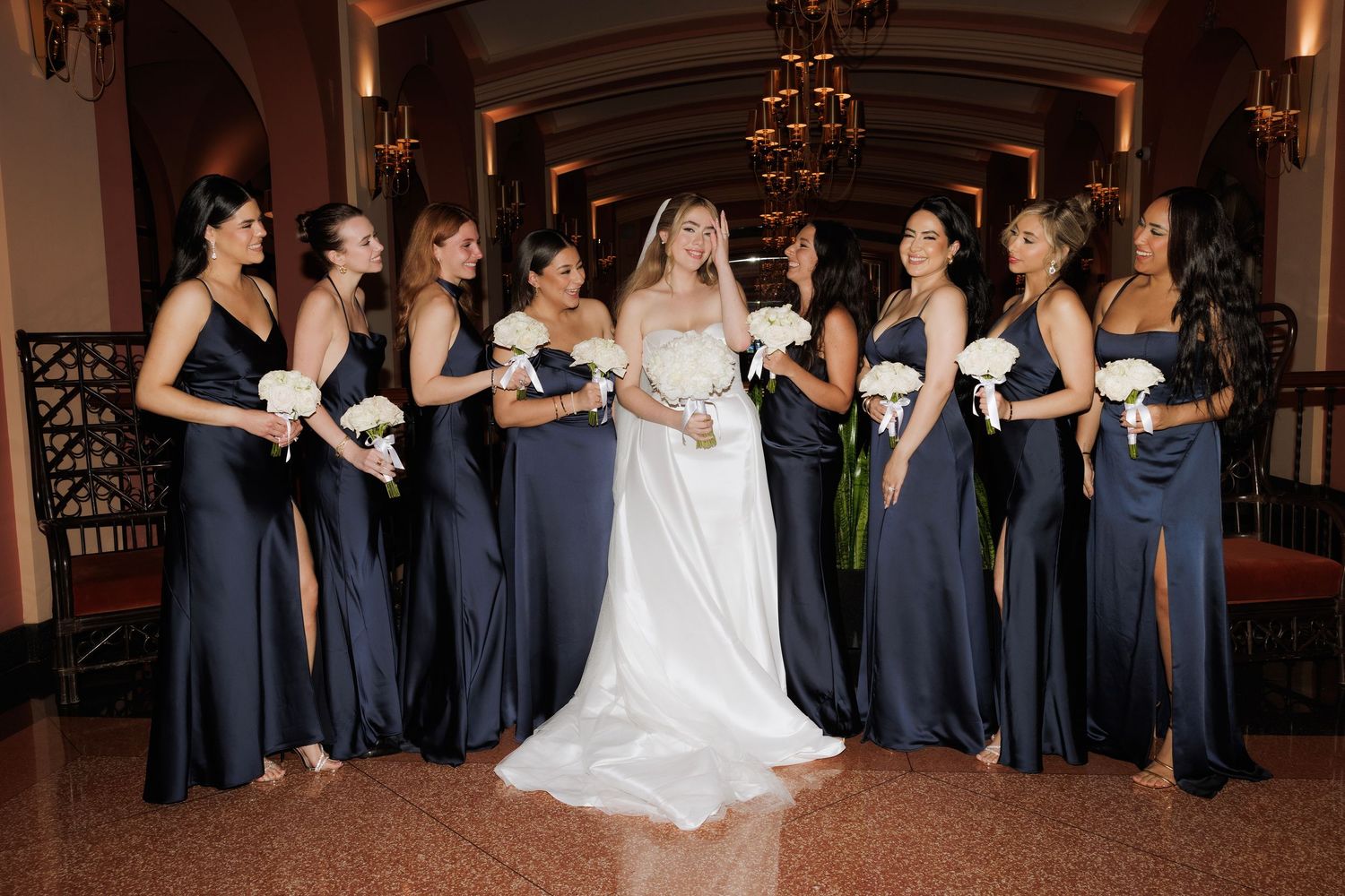 Wedding party members in navy blue dresses dance together in an elegant indoor venue during a celebration.
