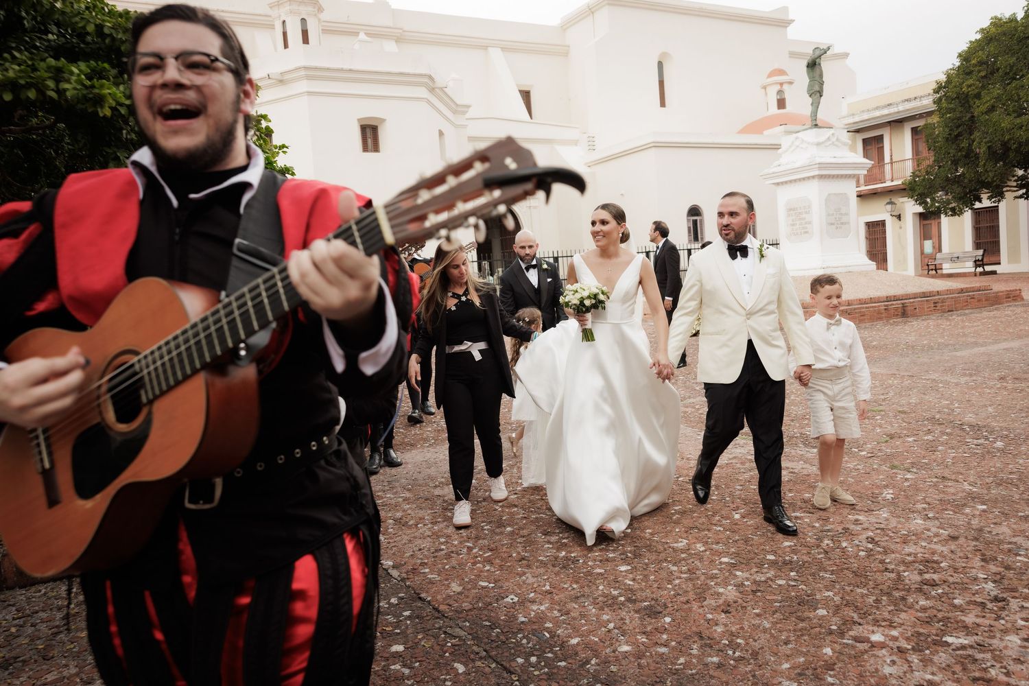 Wedding party walking down a cobblestone street with musicians playing guitars.
