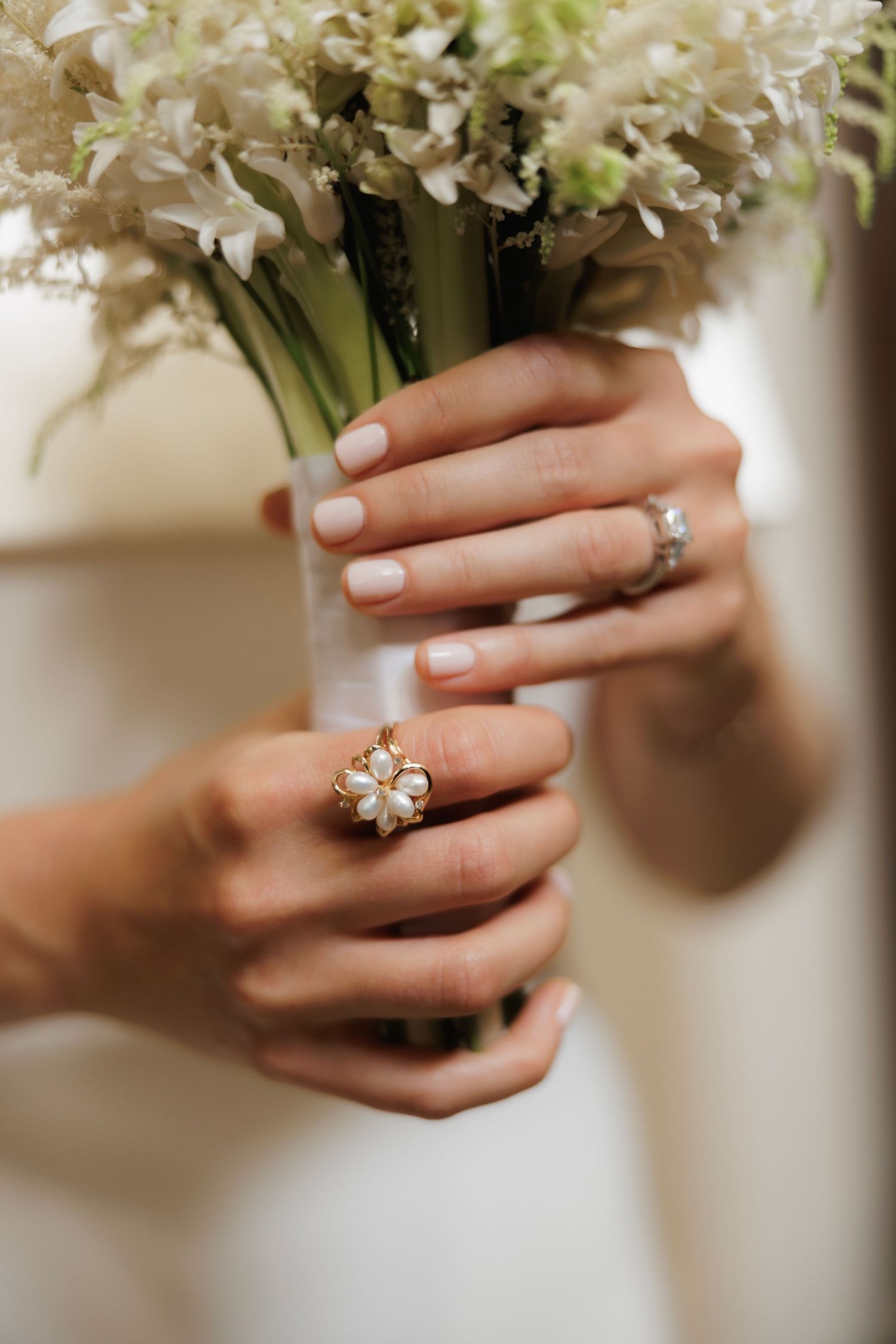 Close-up view of hands holding white flowers while wearing an elegant engagement ring with diamond details.