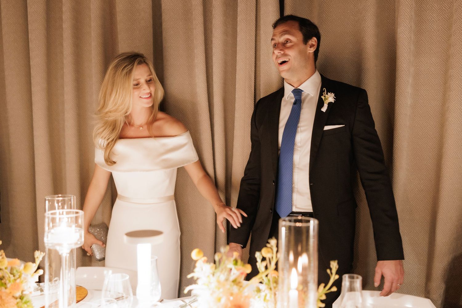Newlywed couple standing at their reception table adorned with glowing candles and elegant decor.