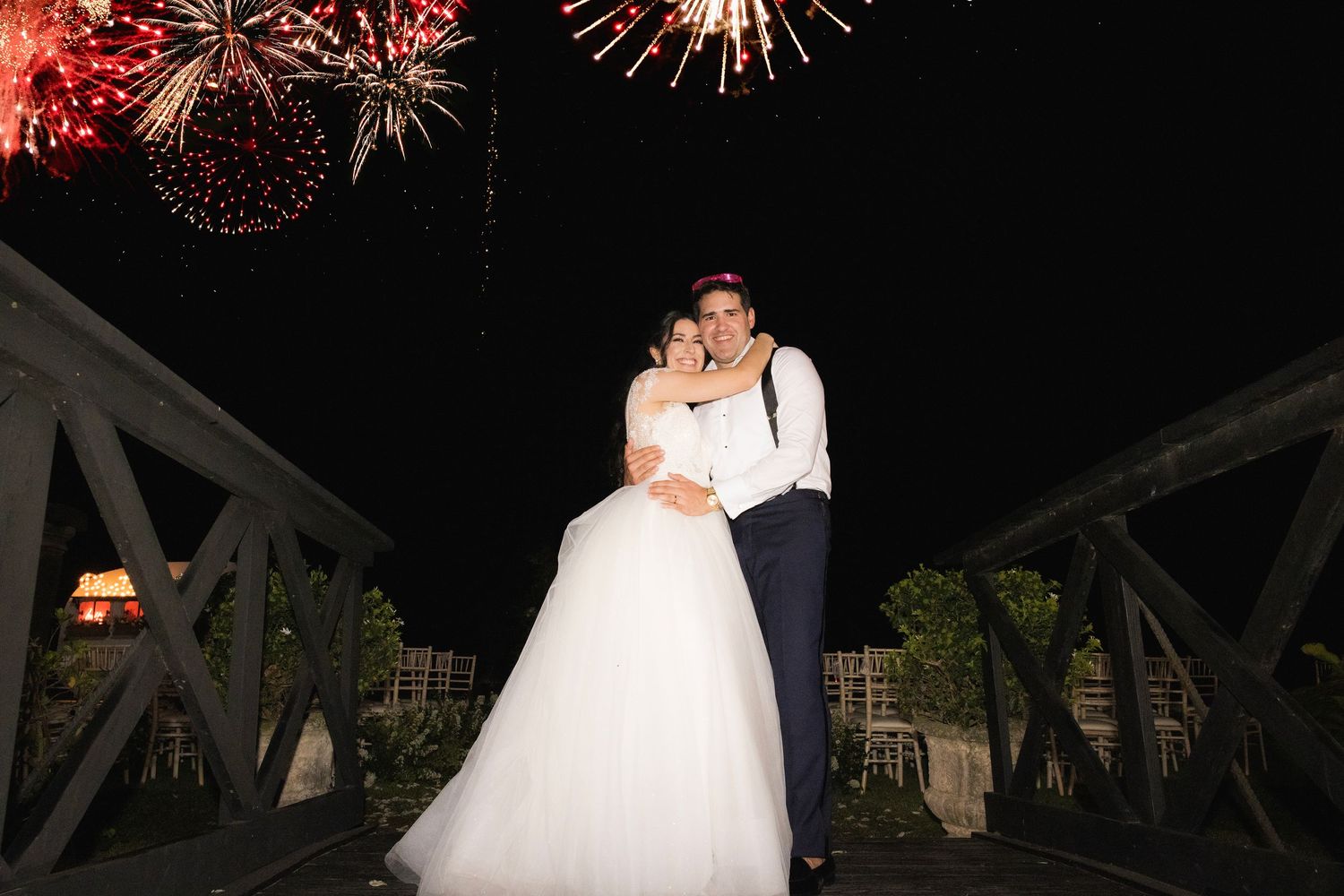 Wedding celebration under the stars with fireworks display bursting in vibrant red colors.