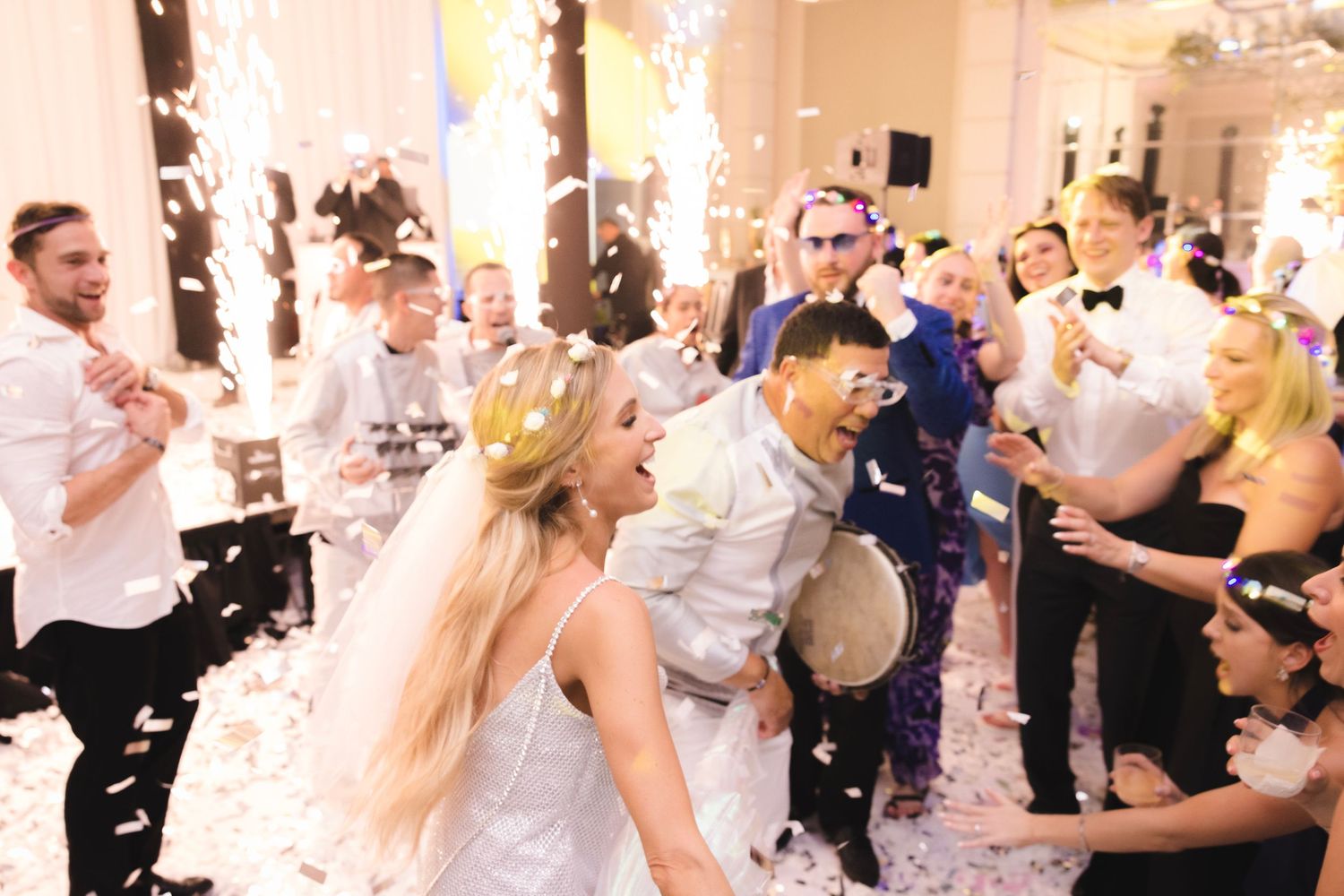 Wedding party dancing and celebrating with confetti falling in an elegant white ballroom reception venue.