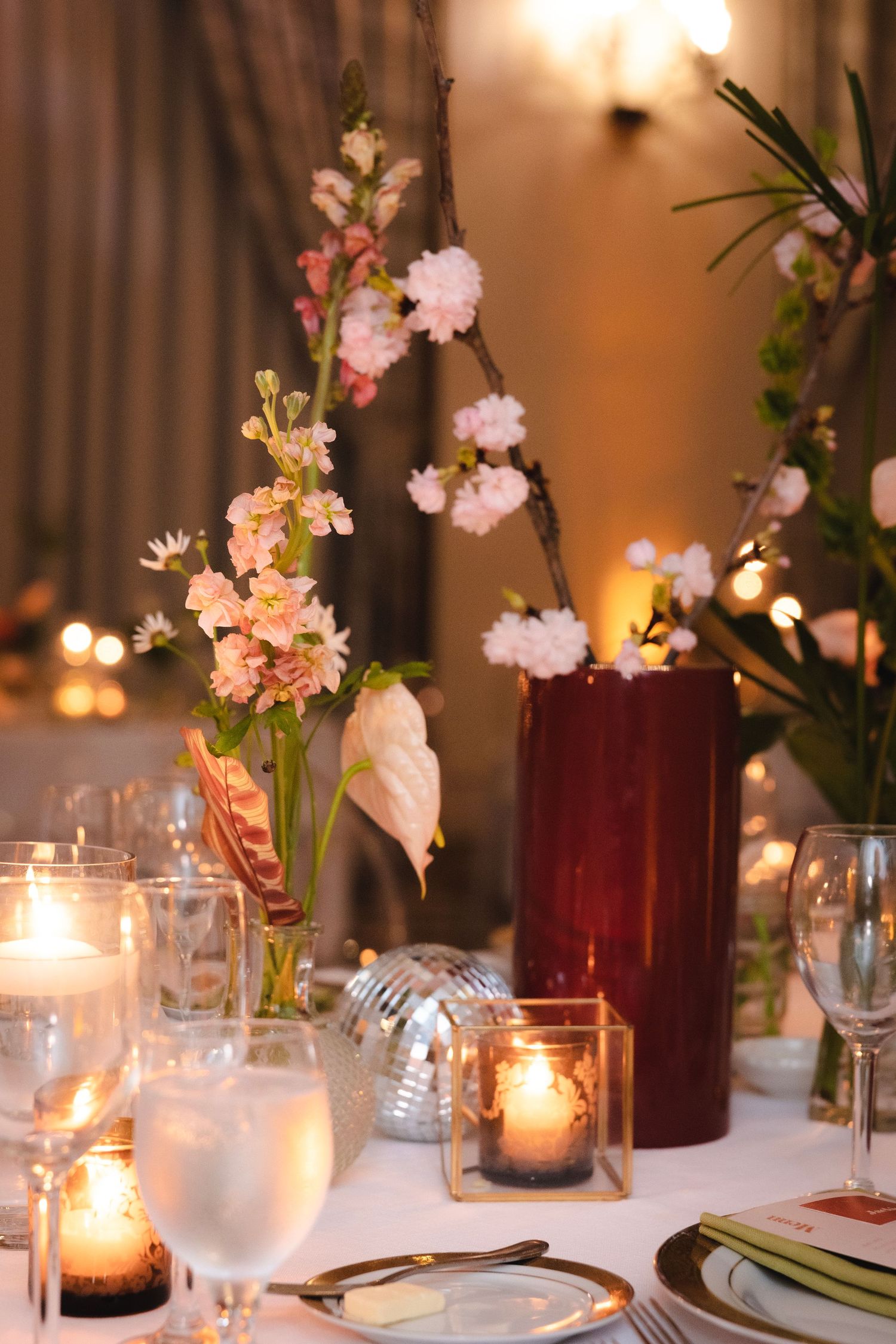 Elegant table setting with pink floral centerpieces, candlelight, and burgundy vases at a formal dinner.