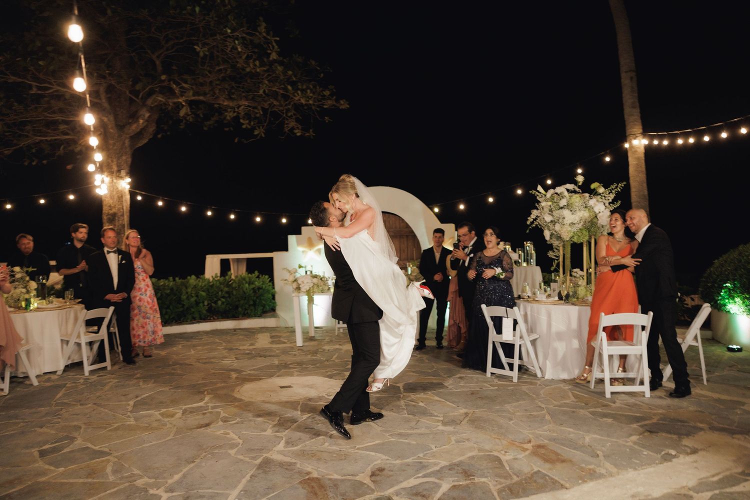 A silhouetted couple performs a romantic dance dip on an outdoor dance floor at a nighttime wedding reception.