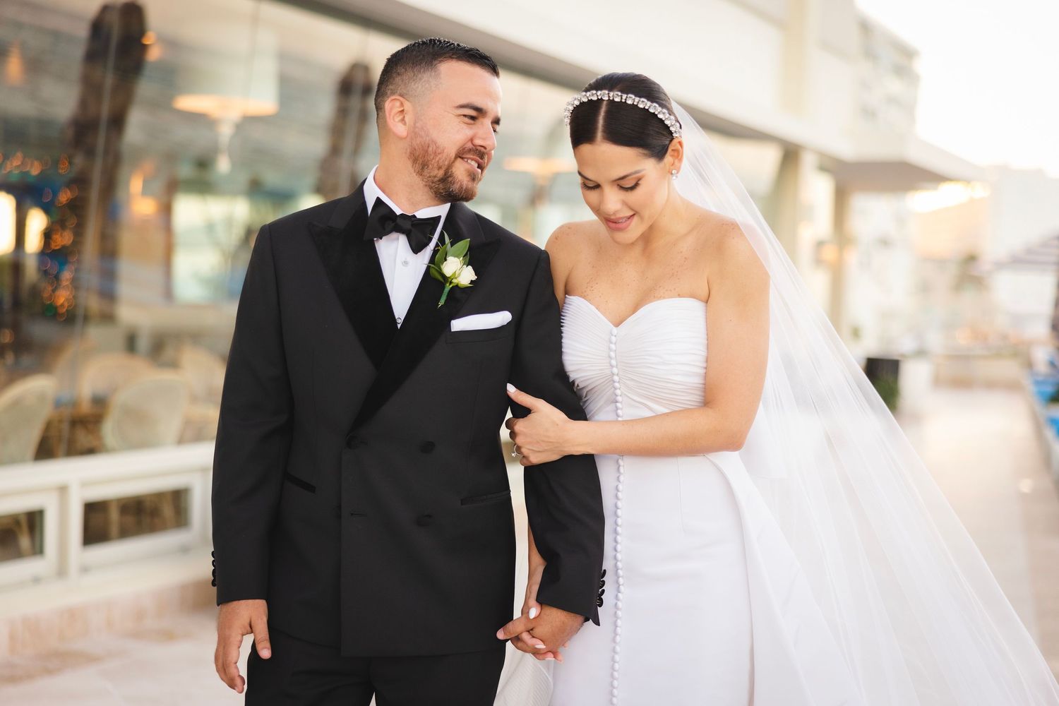 Elegant wedding couple walks happily together through a bright hallway at their luxury hotel venue.