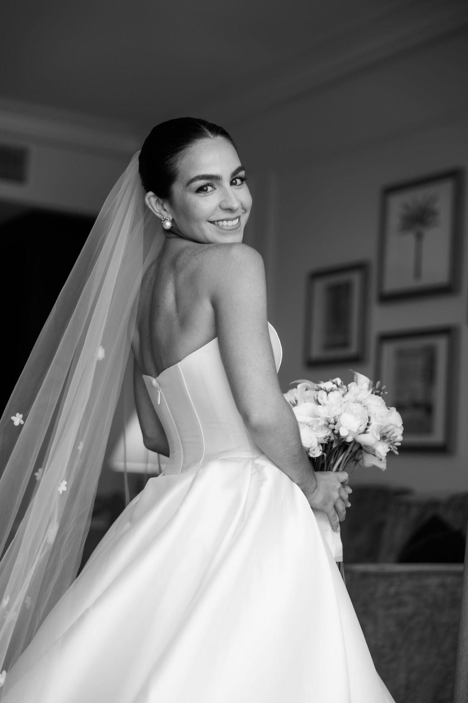 A bride in an elegant white ball gown poses with her veil flowing behind her.