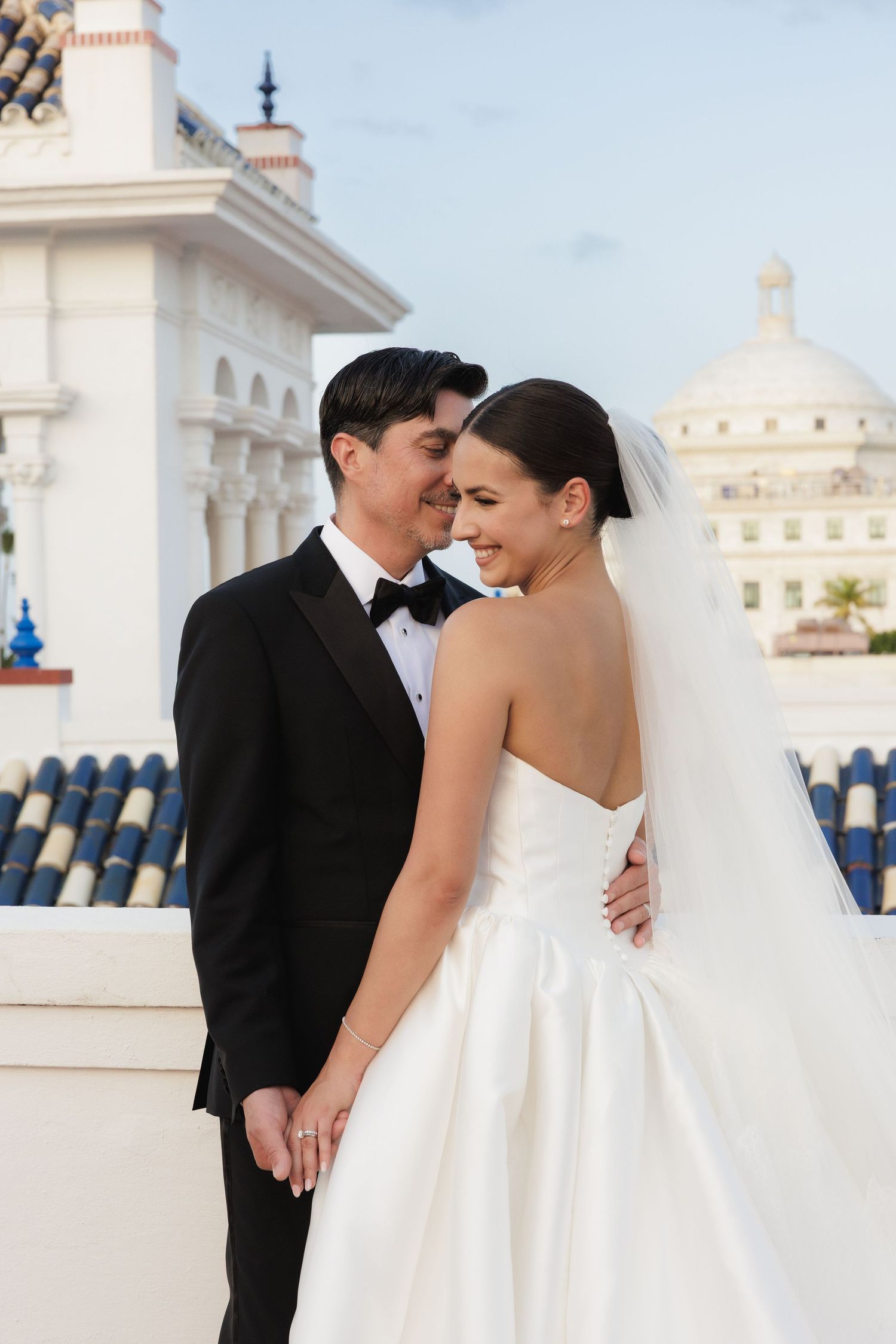 Wedding couple poses against white Mediterranean architecture with domed roofs.