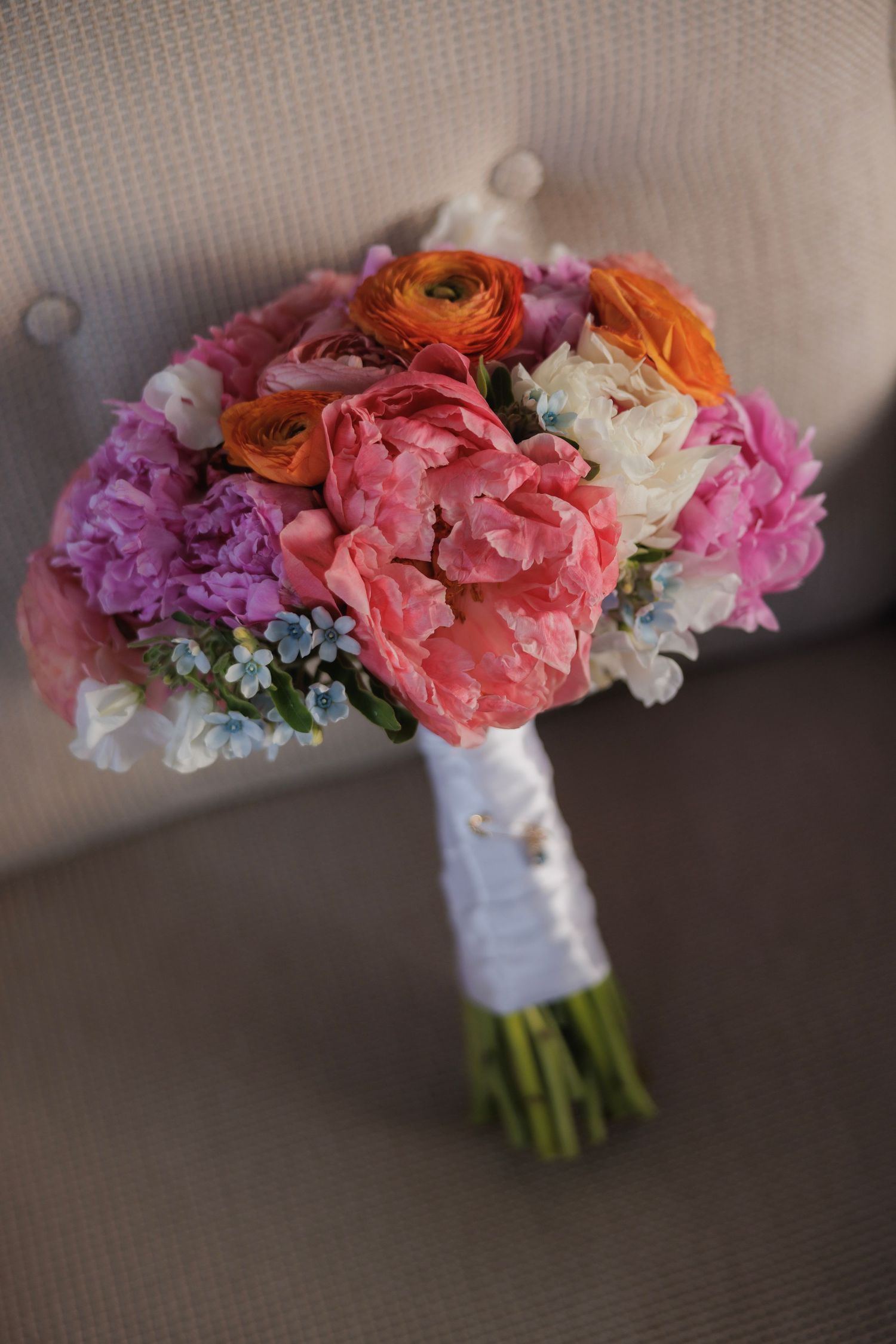 Four wedding bouquets with pink, purple, and orange flowers wrapped in white ribbon lay side by side on a textured surface.
