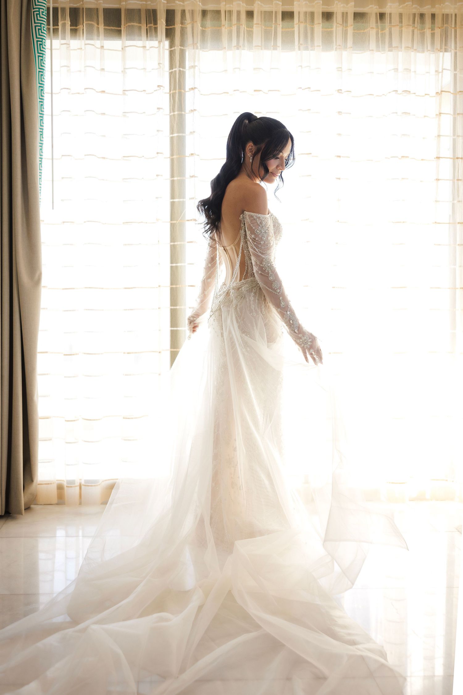 An elegant wedding dress photographed in silhouette against a bright window.