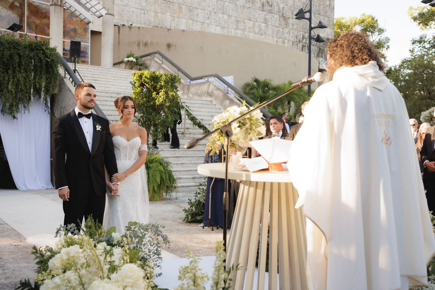 Wedding guests gather on an outdoor stone patio in elegant attire during a sunset celebration.