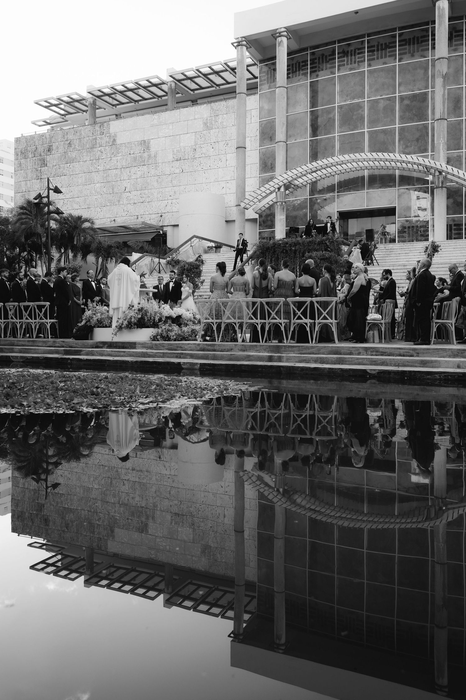 Modern building architecture reflected in a still pool of water with wedding guests gathered.