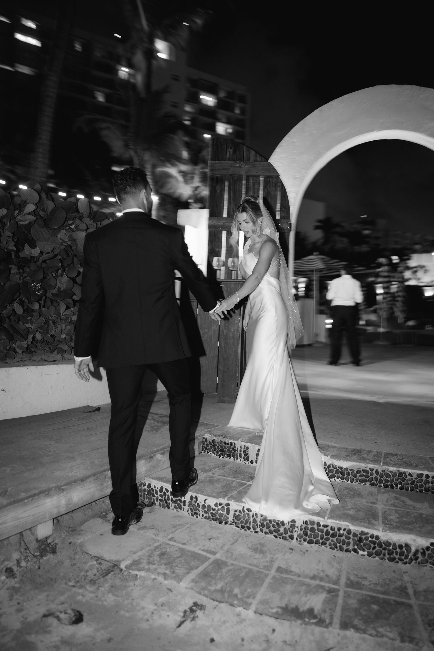 A black and white sequence of a couple in formalwear walking up stone steps at night.