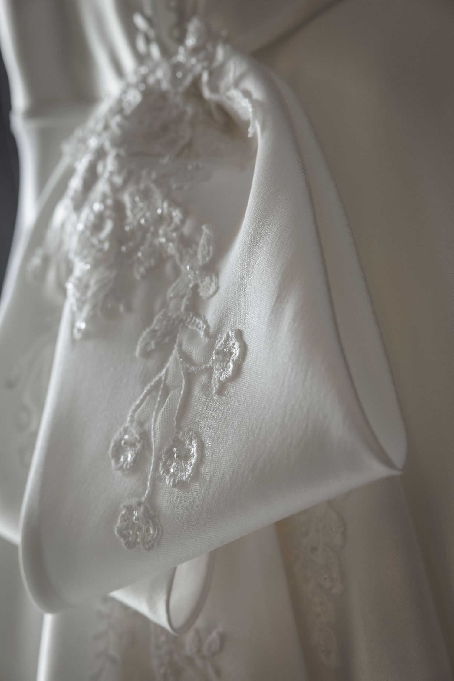 Close-up details of delicate white lace embroidery on wedding dress fabric showing intricate floral patterns.