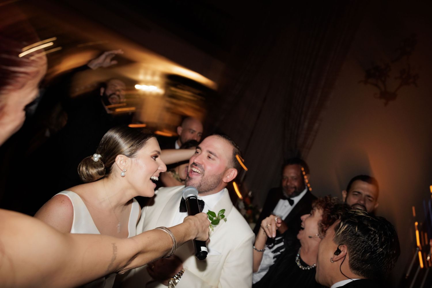 Wedding guests dance and celebrate together on a dimly lit dance floor at a reception party.