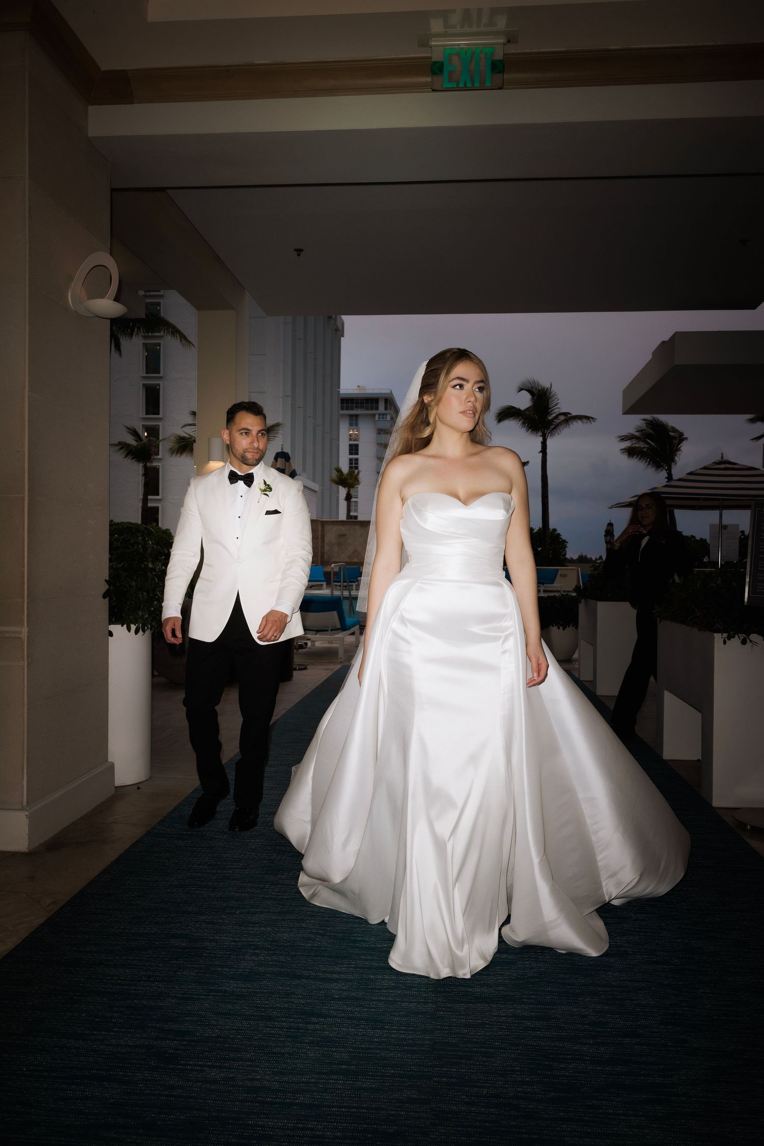 Wedding couple dances together in a dimly lit ballroom with elegant white attire creating a romantic silhouette.