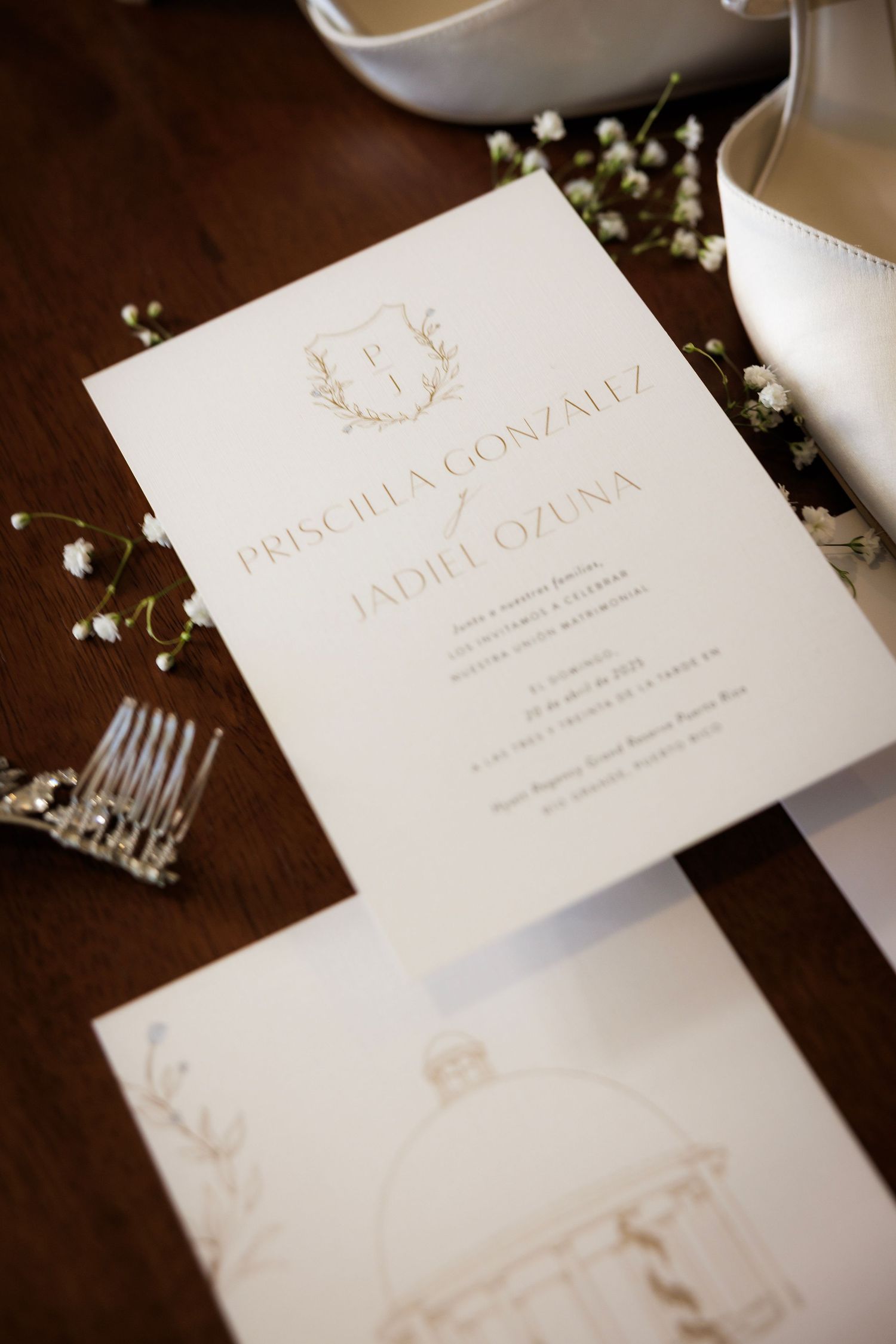 Multiple elegant white and gold wedding invitation cards arranged on a dark wooden surface with baby's breath flowers.