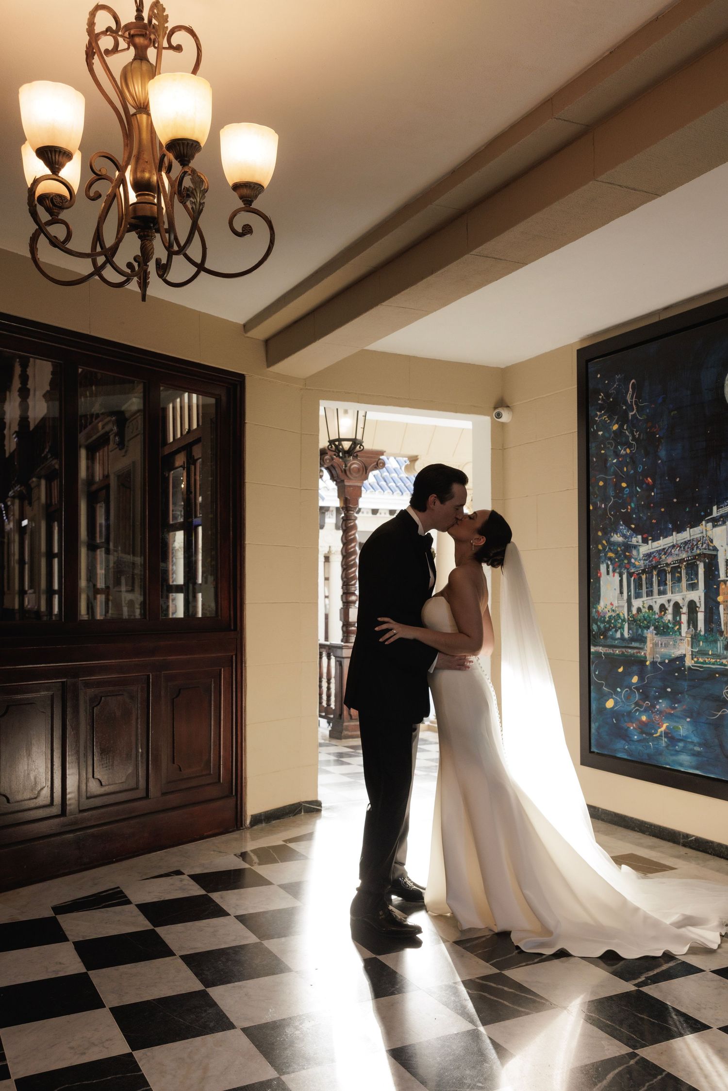 Silhouetted couple embracing in an elegant indoor hallway with checkered floors and dramatic lighting.