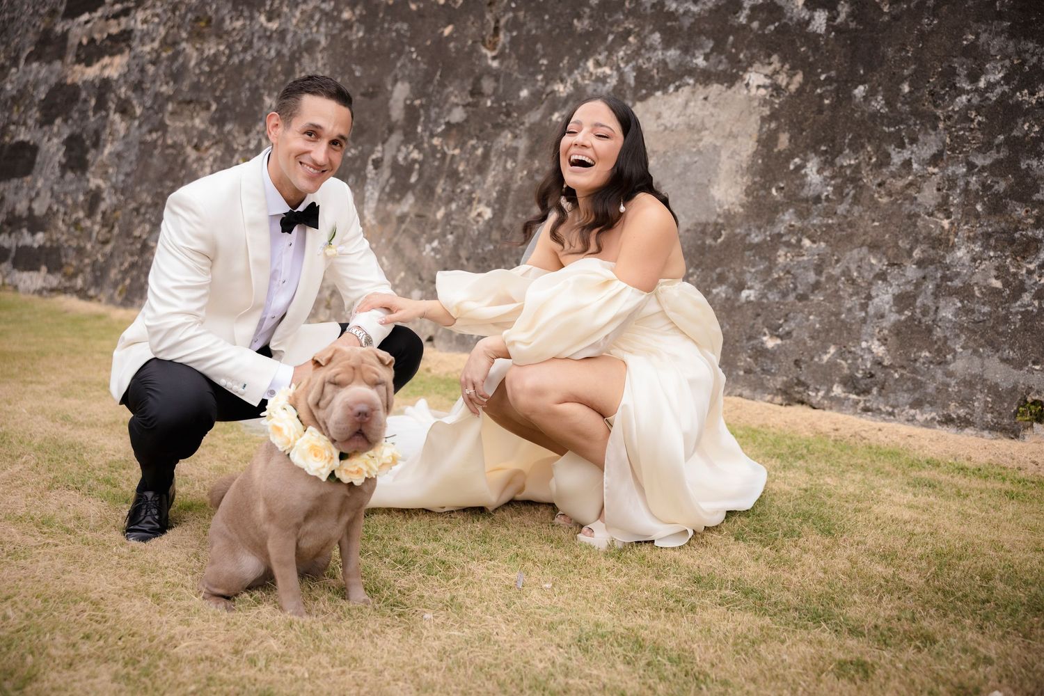 Candid moments of newlyweds playing on grass against stone wall backdrop.