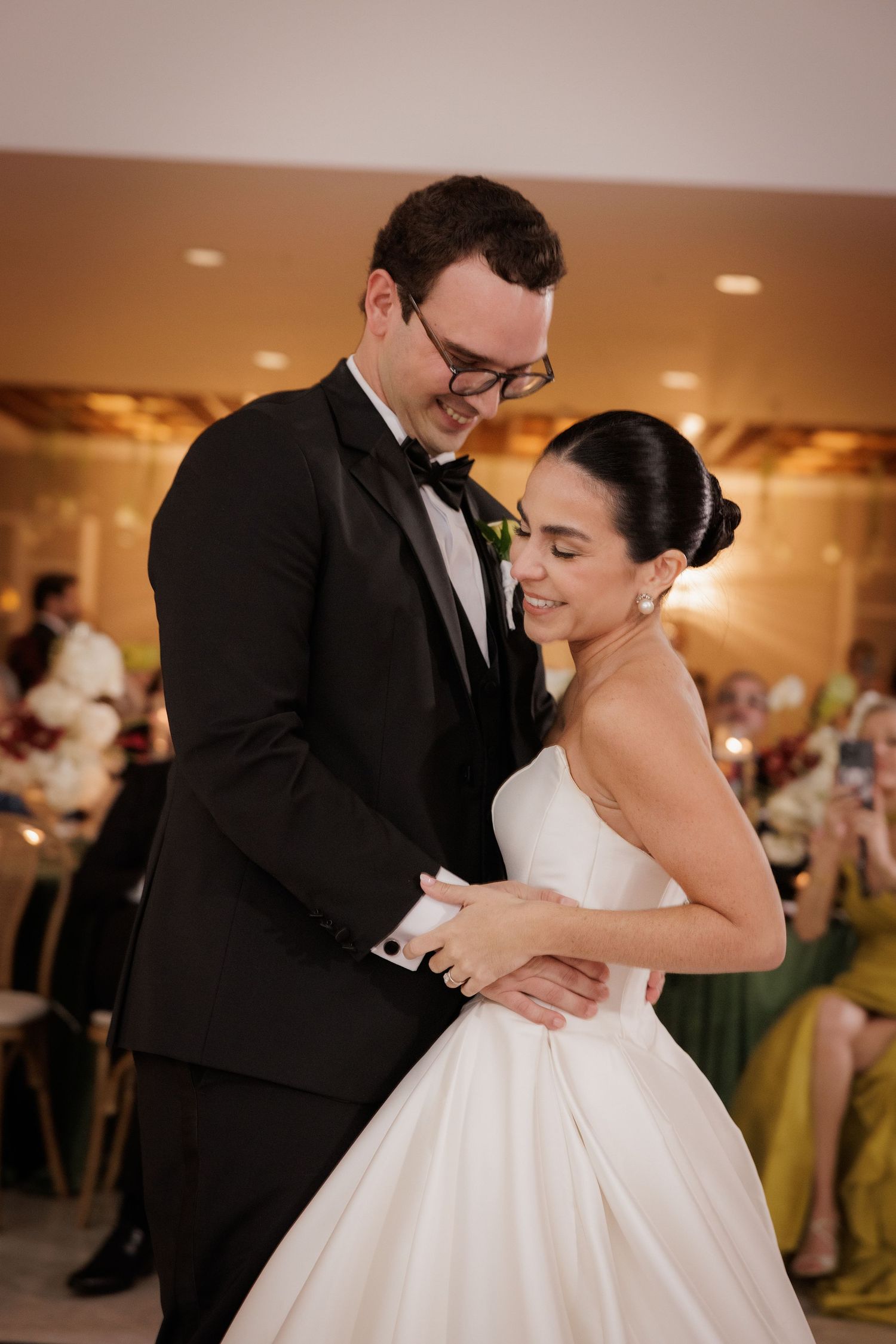A couple shares an intimate first dance at their wedding reception in a warmly lit ballroom.
