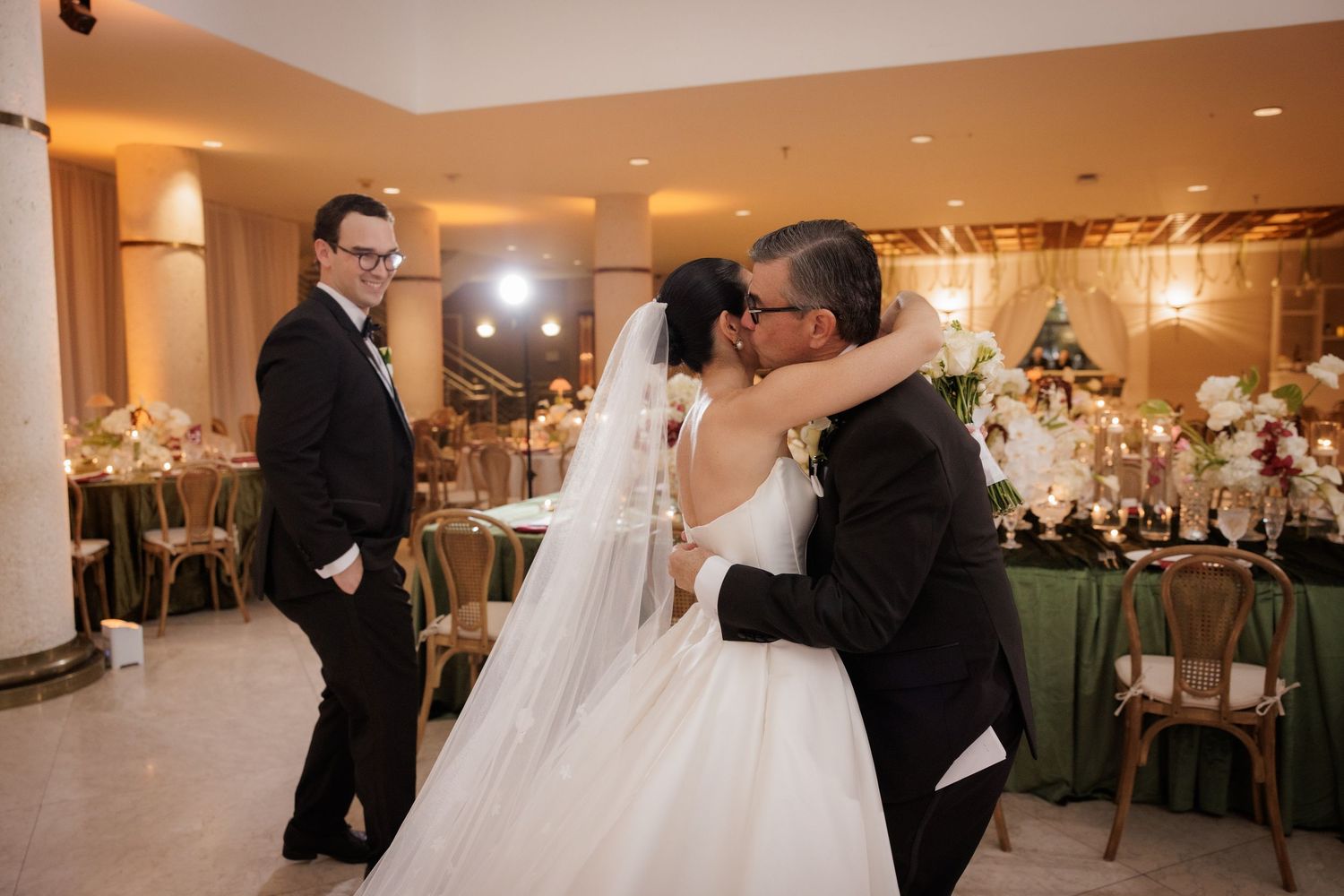 Wedding reception guests dance and celebrate on an elegant ballroom dance floor with warm lighting.