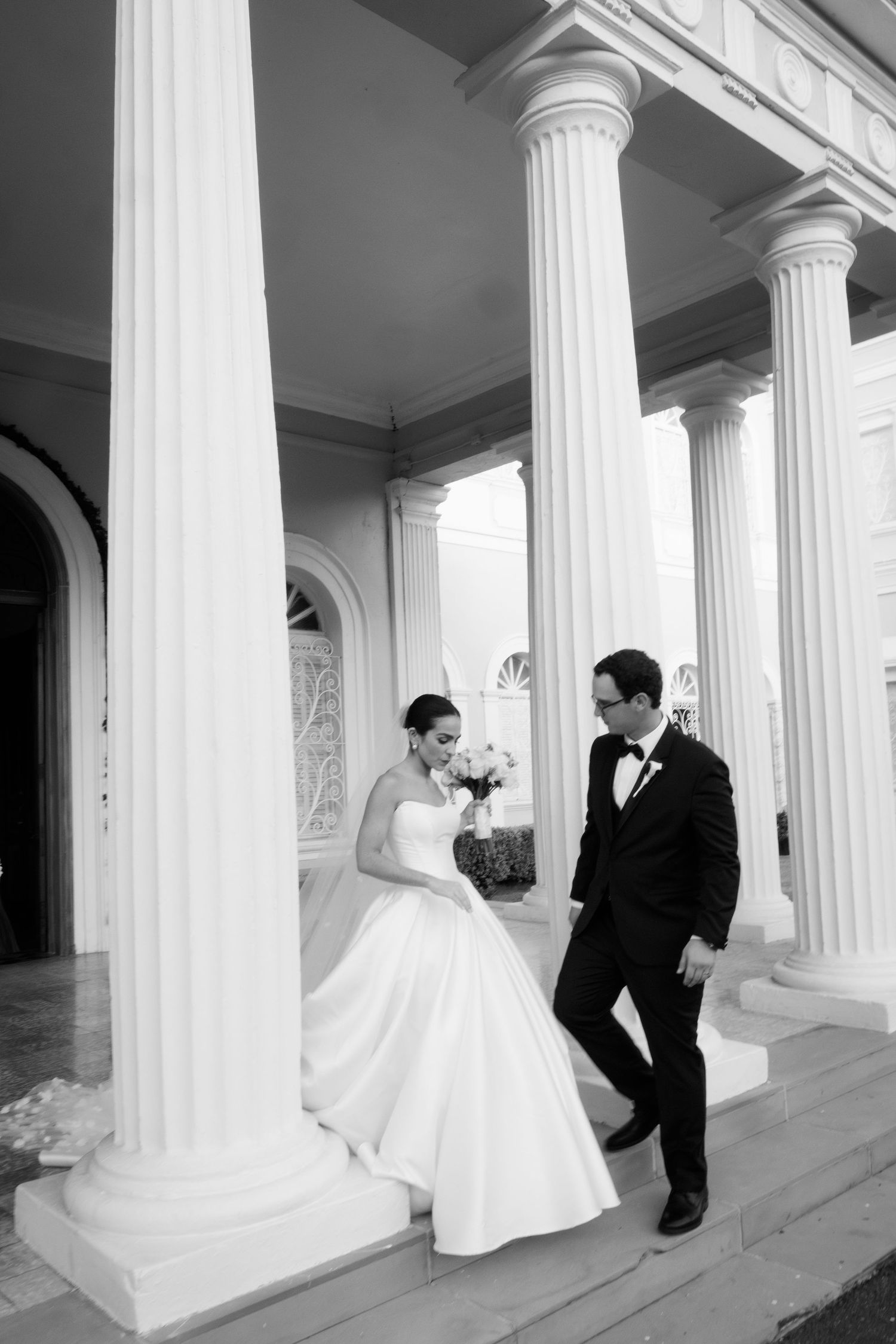 A romantic black and white wedding photo series showing a couple posing between elegant white columns.