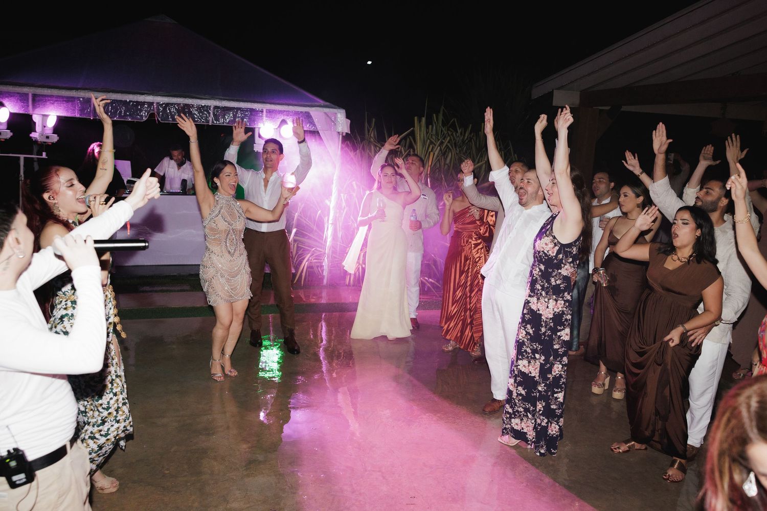 People dancing and celebrating at a nightclub with purple lighting and glowsticks creating an energetic party atmosphere.