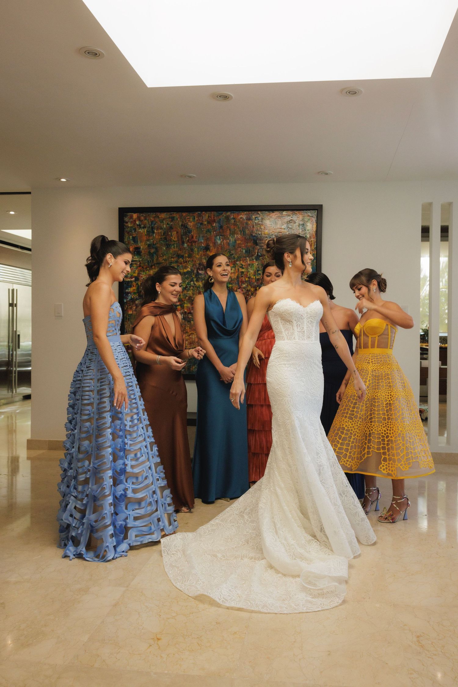 Wedding party in colorful dresses gathered around a bride in a white lace gown.
