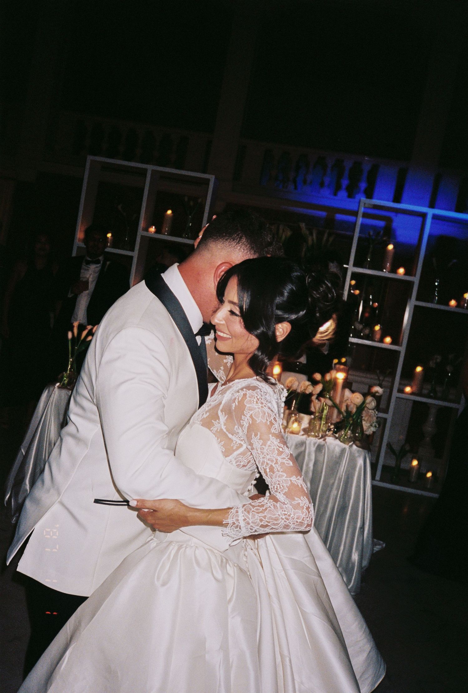 Bride and groom share a romantic first dance embrace at candlelit wedding reception, bride in lace ball gown.