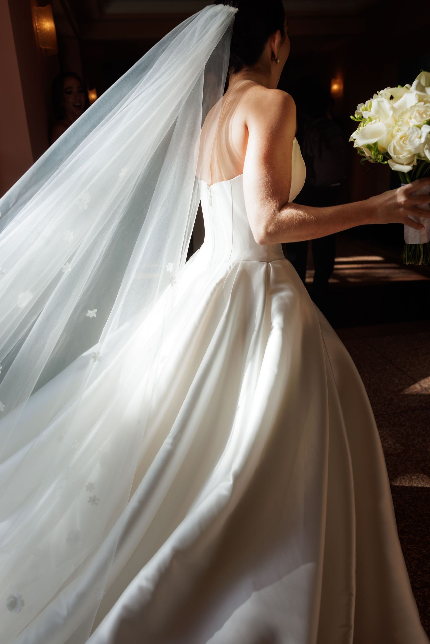 Elegant white wedding dress with flowing train and veil captured in dramatic lighting.