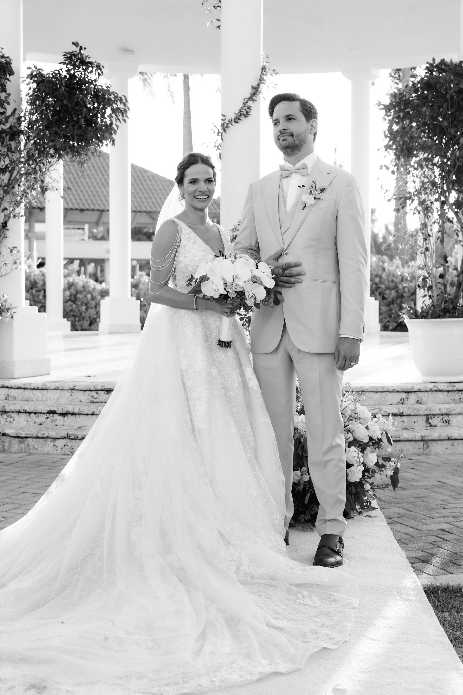 A couple in wedding attire share an intimate moment together on a paved white terrace during their special day.