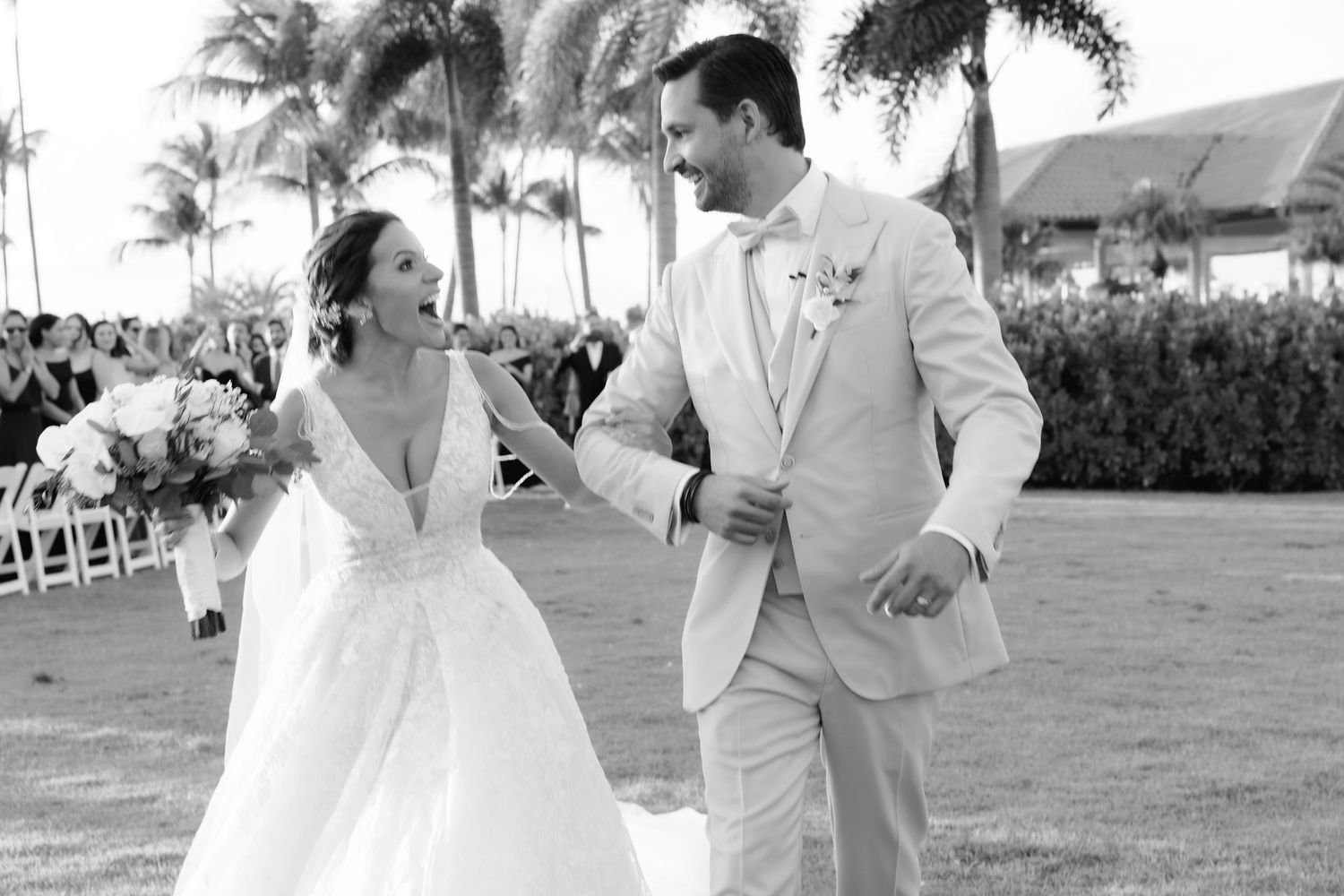 A couple celebrates their wedding day in an elegant outdoor setting with palm trees and tropical scenery in the background.