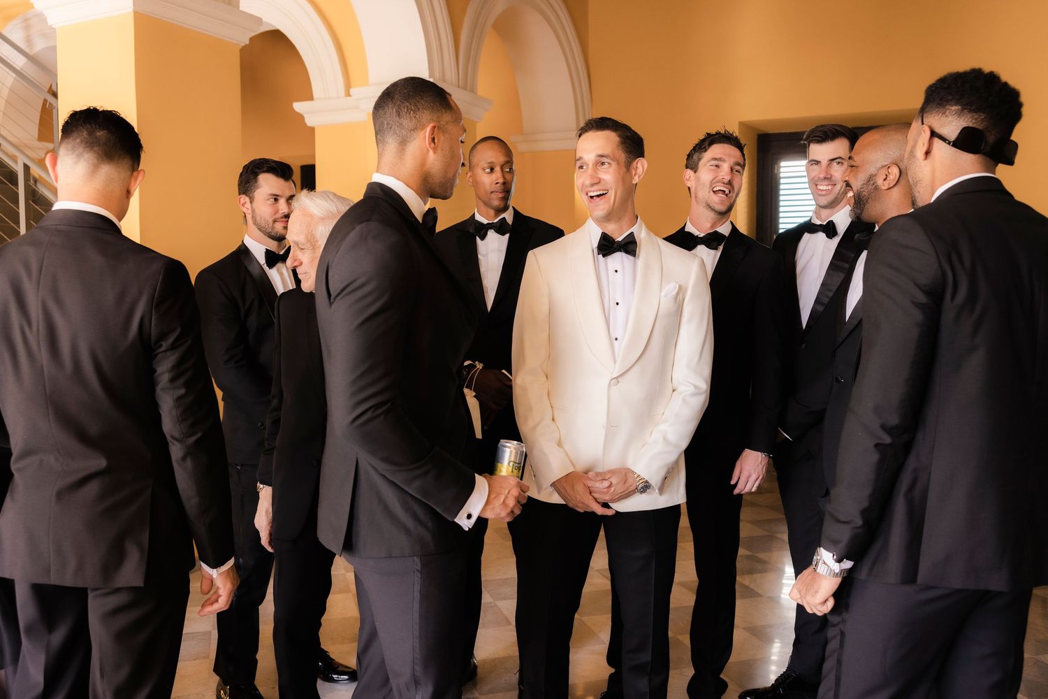 A group of formally dressed people in black suits and white shirts standing against a beige wall during an event.