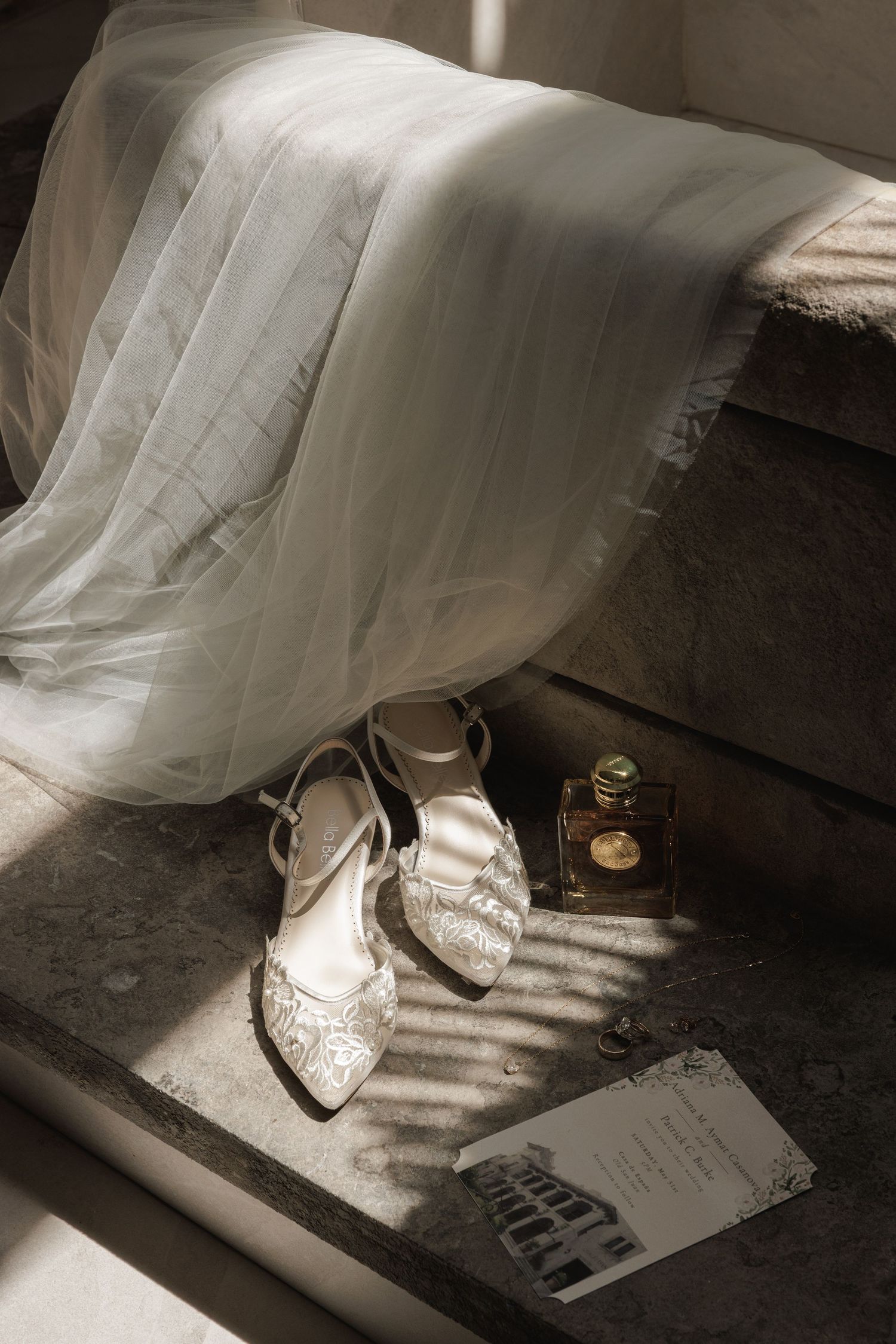 Elegant white bridal shoes sit in dramatic lighting next to a paper on a dark surface.