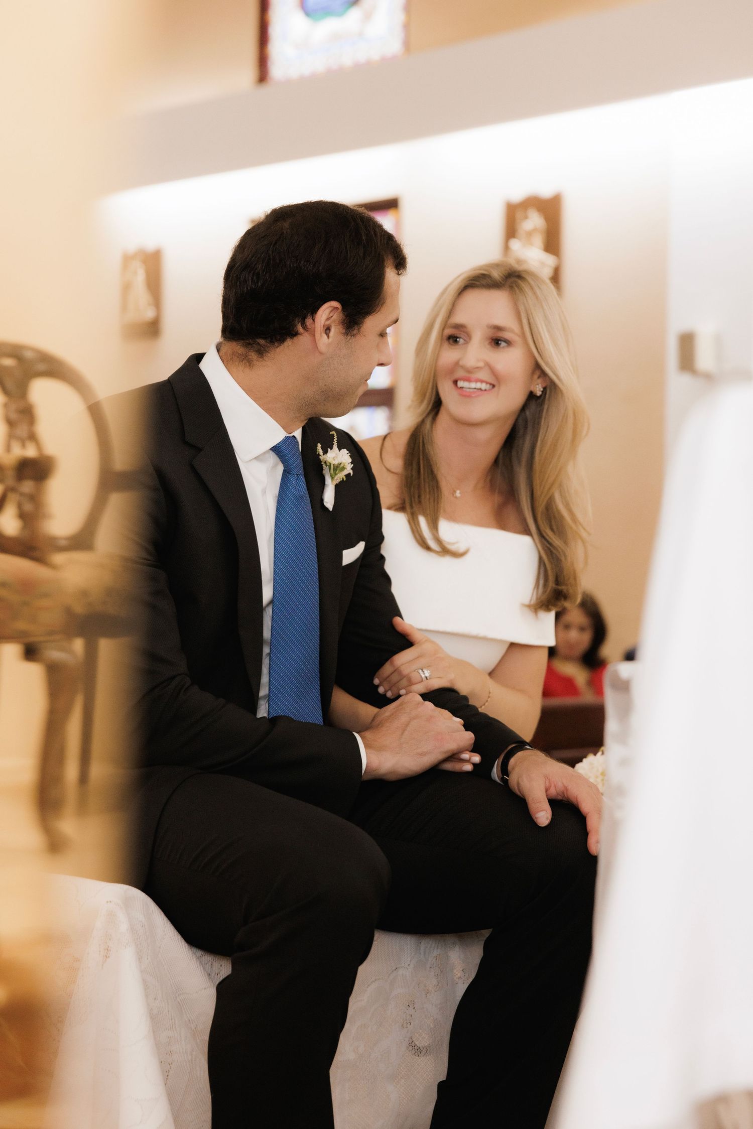 A couple shares an intimate moment at their wedding, the bride in white and groom in a dark suit with blue tie.