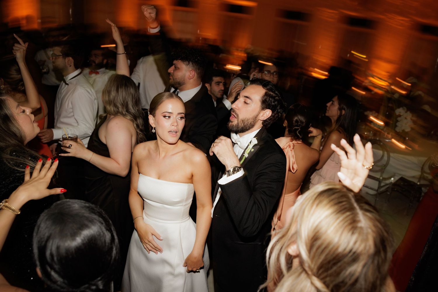 Guests dance and celebrate at a lively wedding reception with warm ambient lighting.