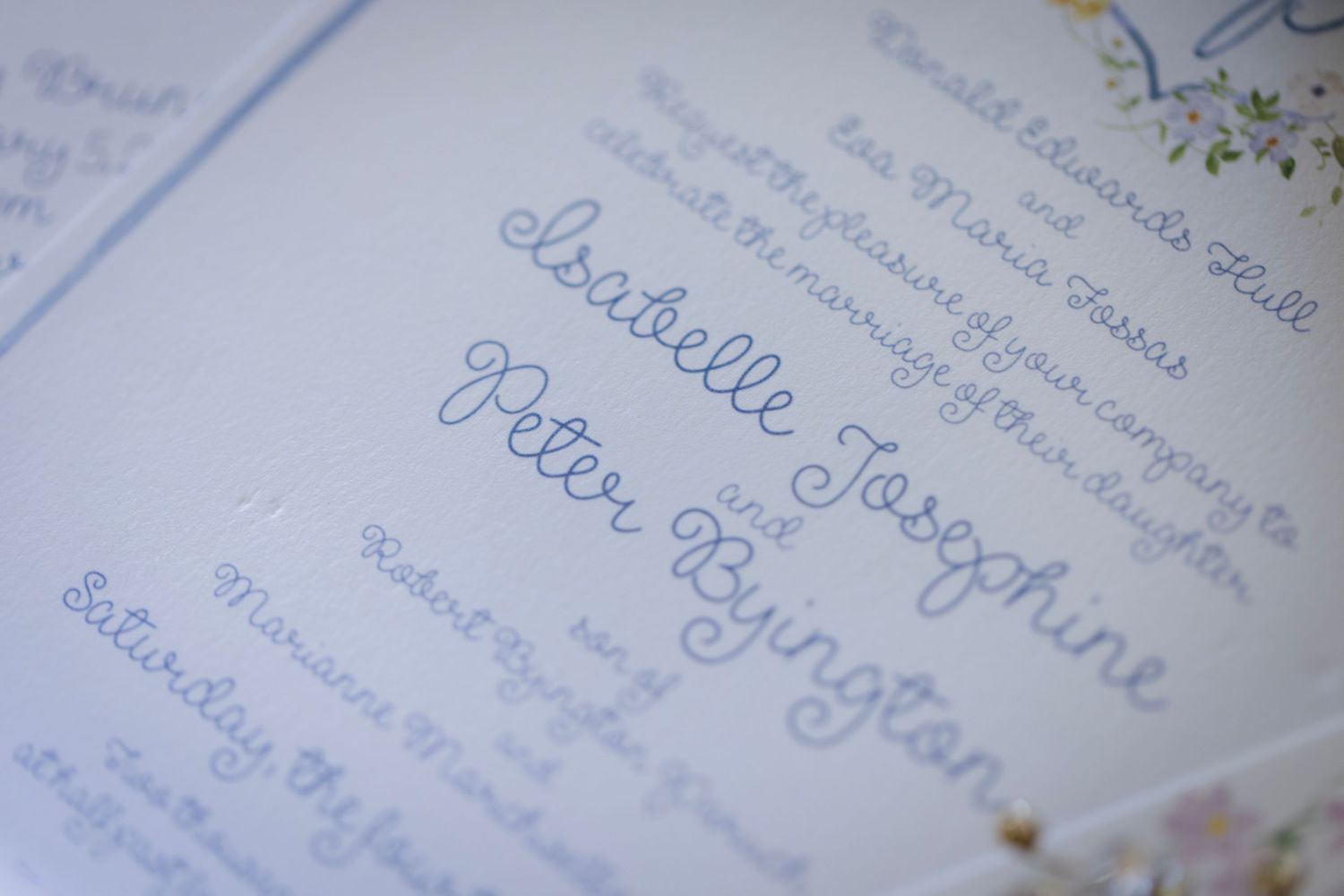 Elegant cursive handwriting in blue ink on textured paper showing wedding details and calligraphy.