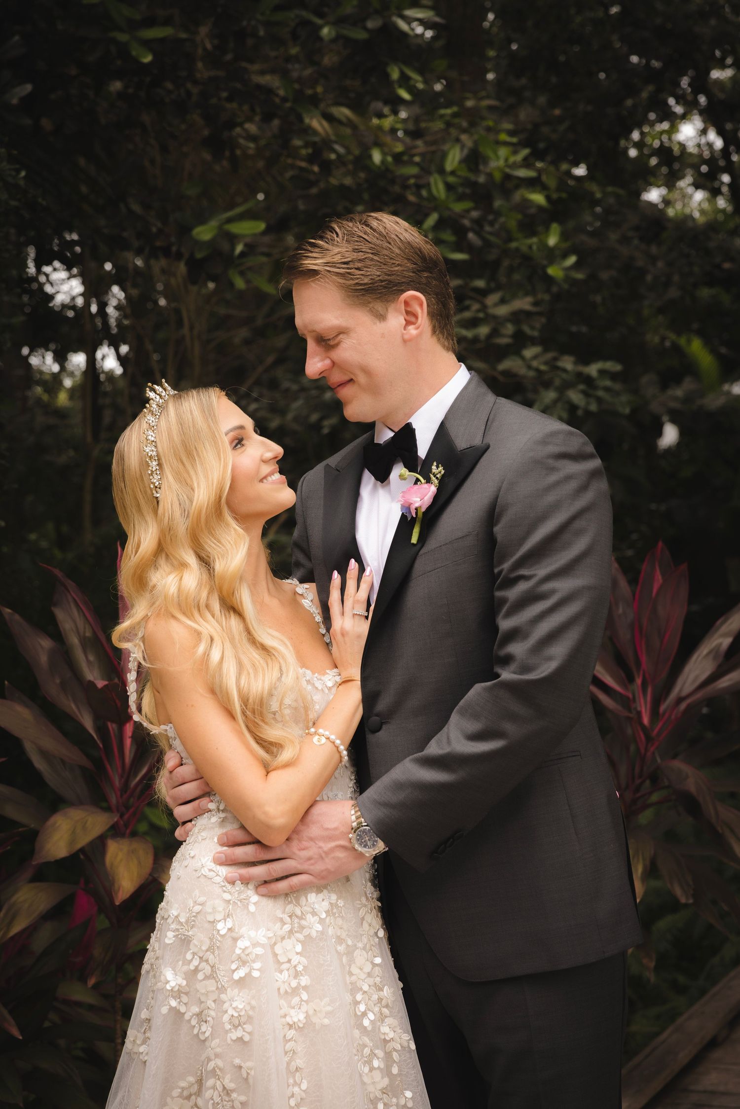 A romantic wedding moment captured in a garden setting with tropical plants in the background.