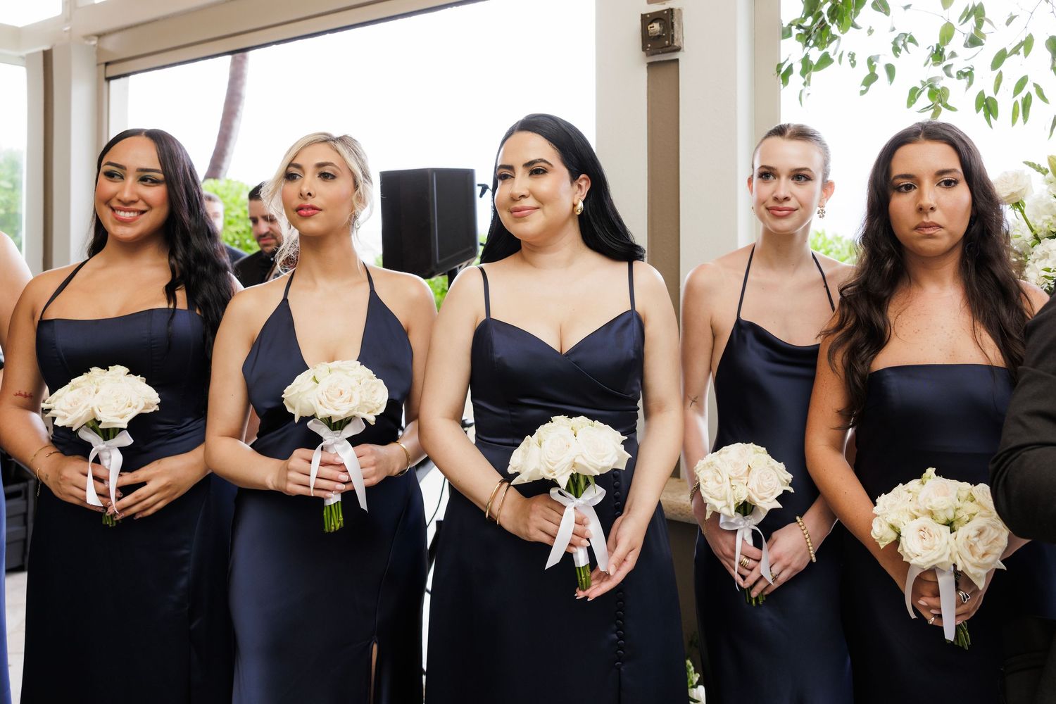 Bridesmaids in black dresses stand in a row holding white bouquets.