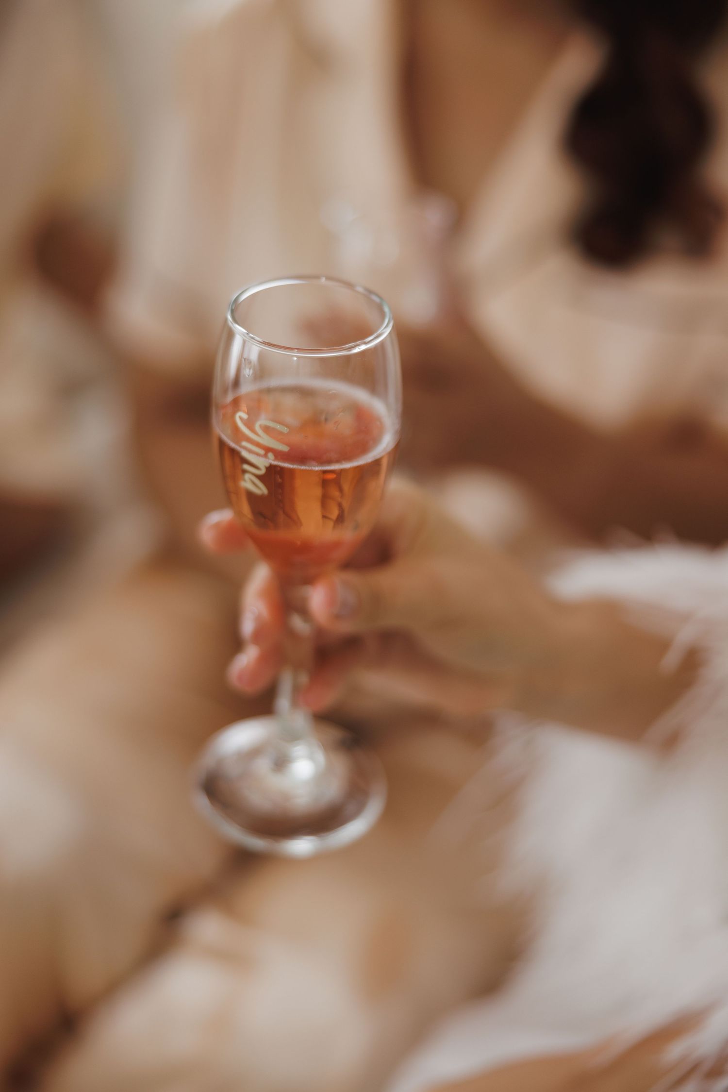 A glass of rose champagne being held against a soft blurred background.