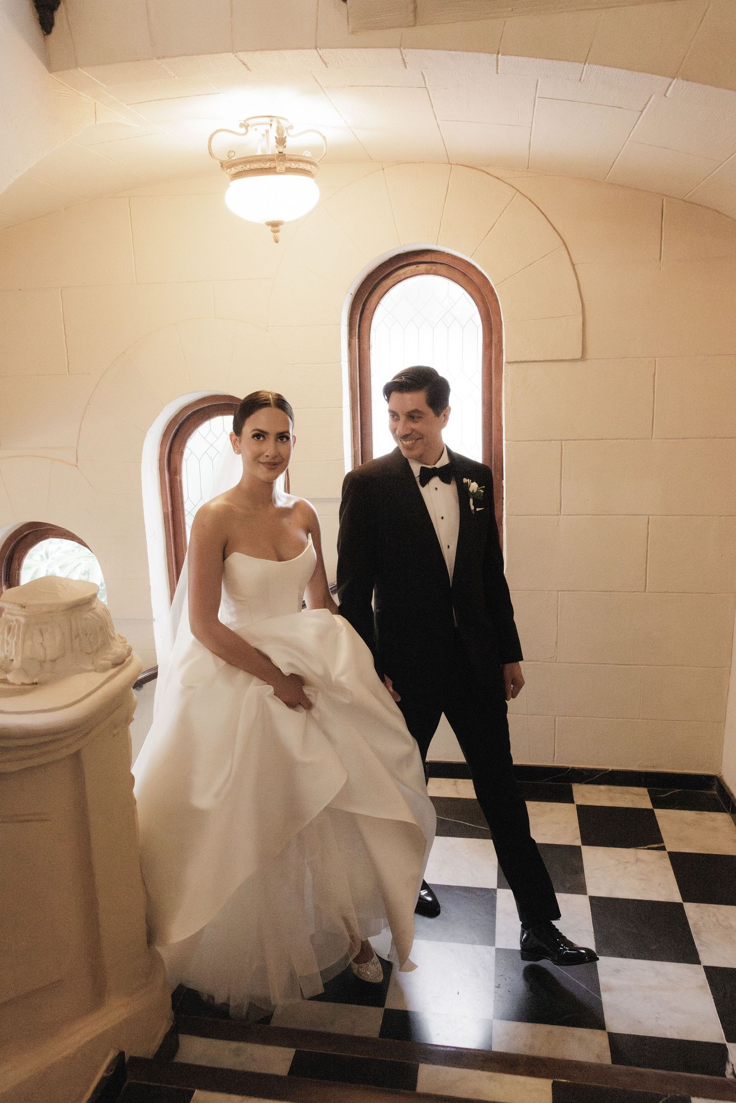 Candid wedding moments captured in a hallway with checkerboard floor and arched windows.