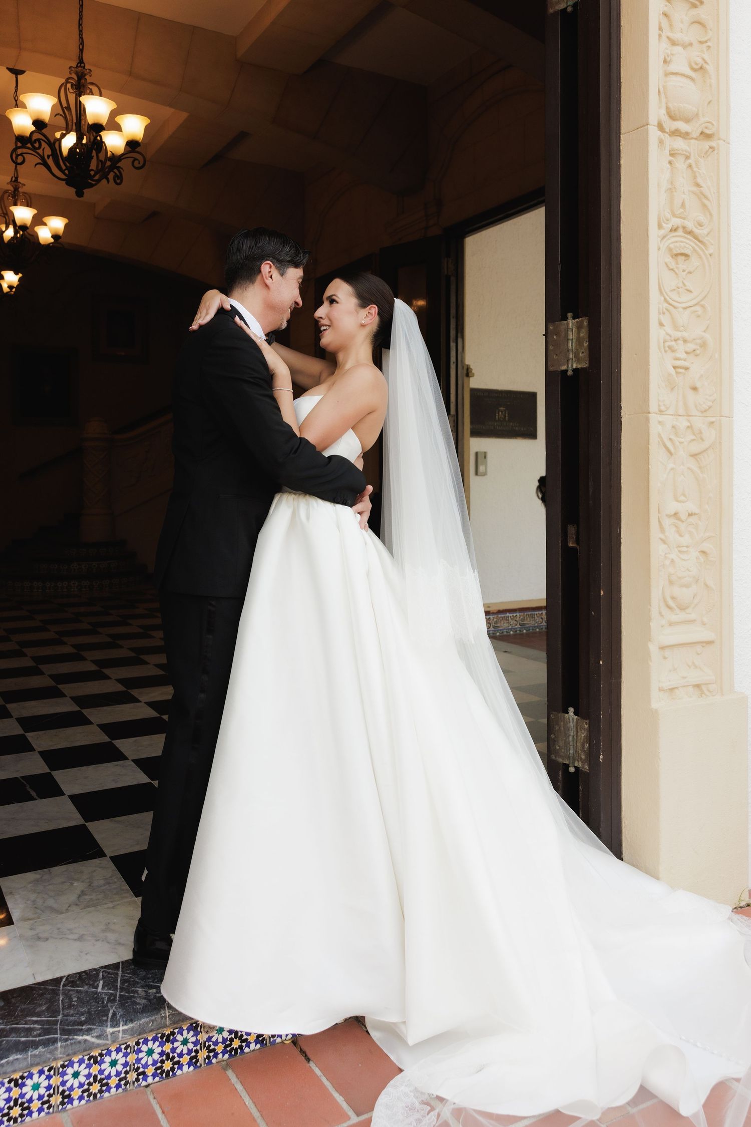 A romantic wedding scene shows a couple dancing together on a black and white checkered floor in an elegant venue.