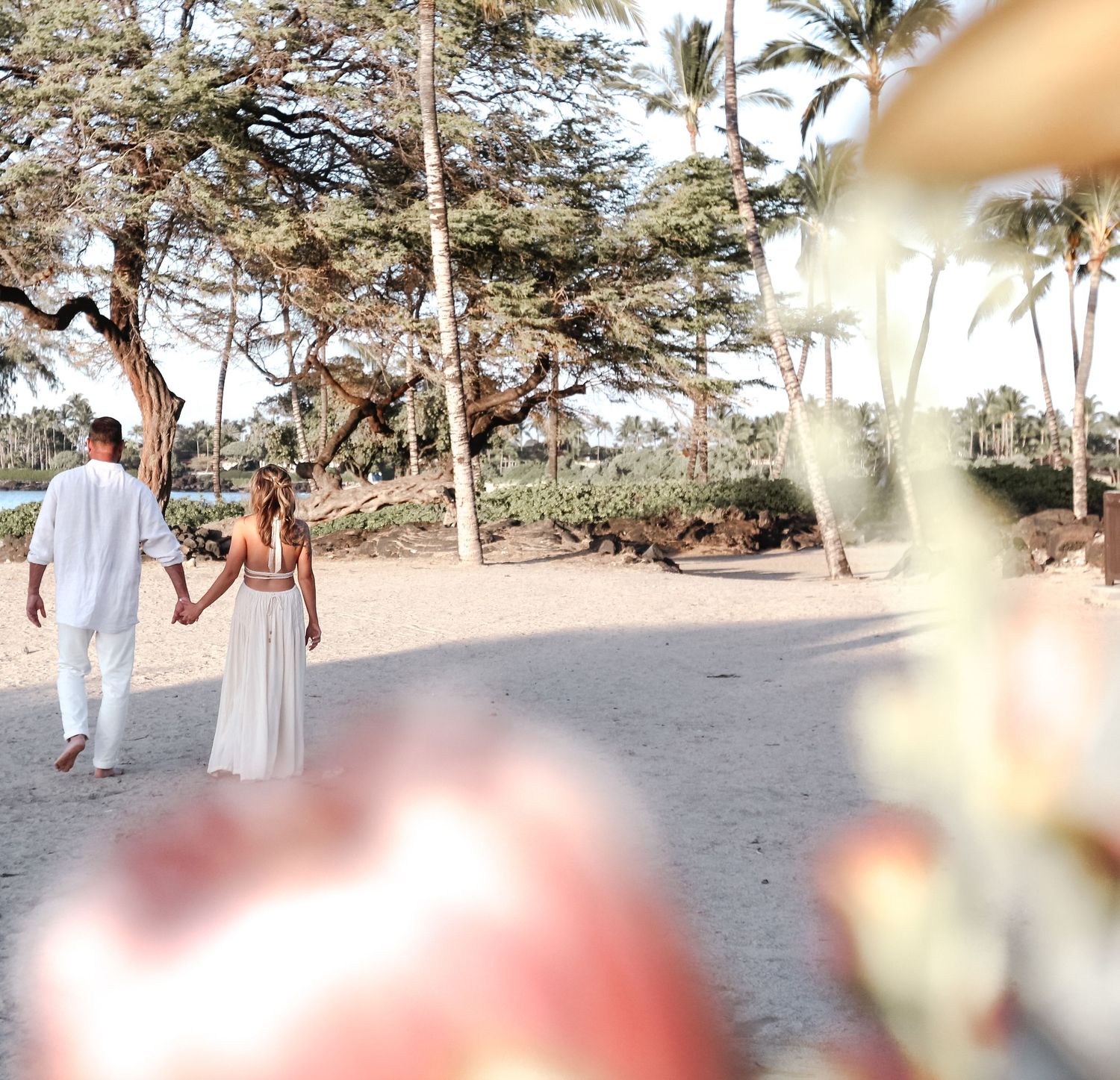 Couple walking at Kukio Beach Hawaii during elopement session with floral viewfinder framing foreground at sunset