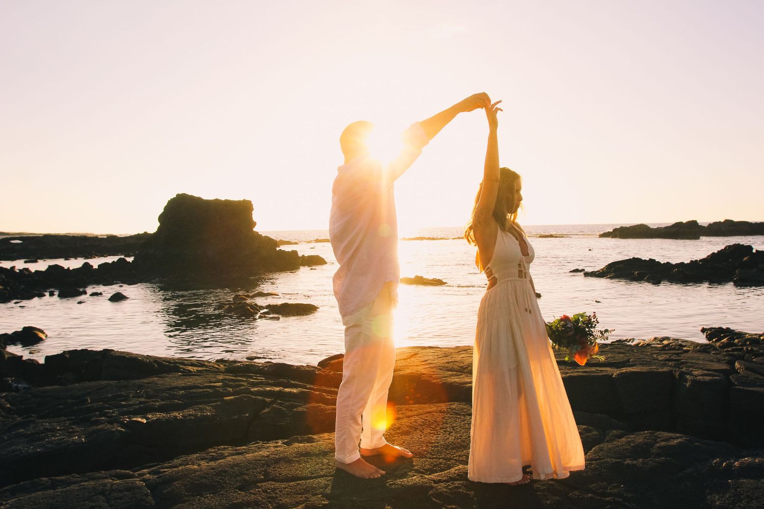 Couple twirling on rocks at sunset at Kaikaua Point Beach Park Kona Hawaii with ocean and golden light backdrop