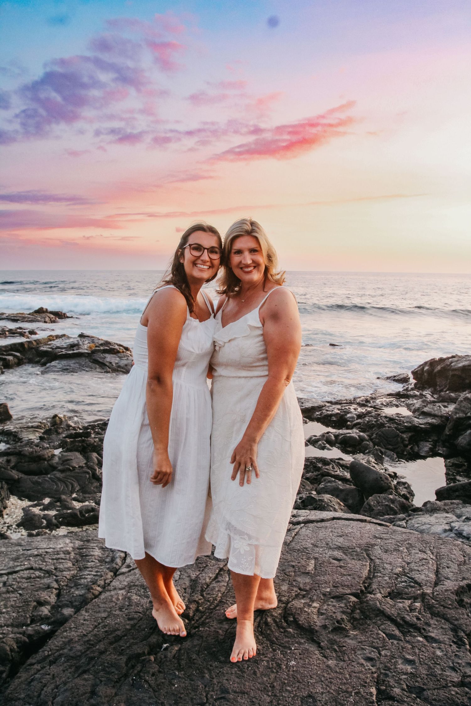 Sunset mother and teenage daughter session on rocks in Kona Hawaii with pink sky and ocean backdrop